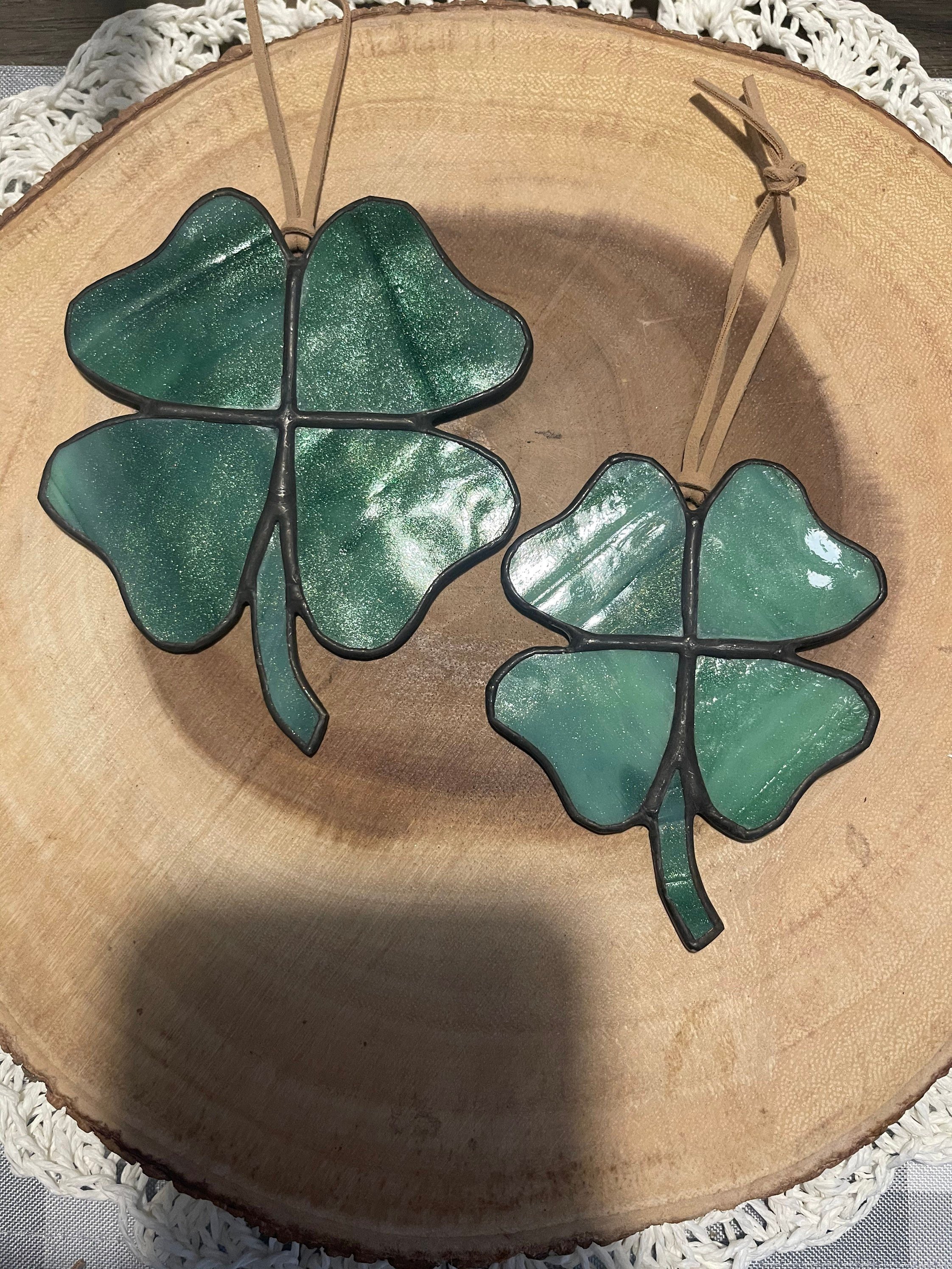 Two decorative green glass four-leaf clover shaped dishes inside a wooden bowl with a lace napkin underneath.