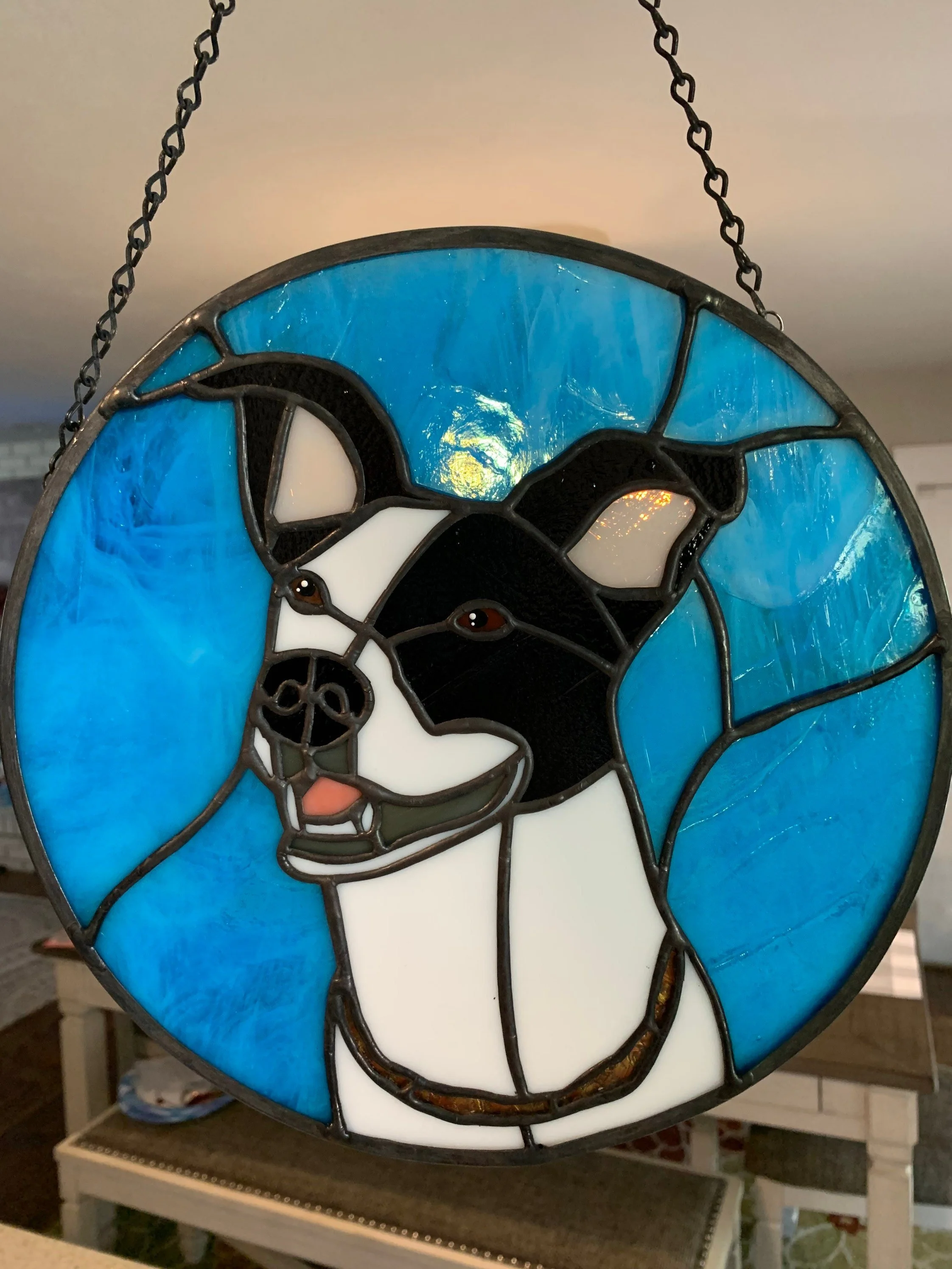 Stained glass lamp featuring a dog, with black, white, and brown colors, set against a background of bright blue stained glass.