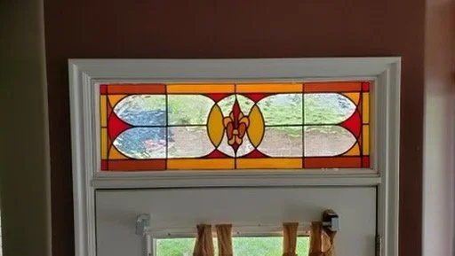 Close-up of a stained glass window featuring red, yellow, orange, and green colors with a symmetrical design, positioned above a door with a curtain.