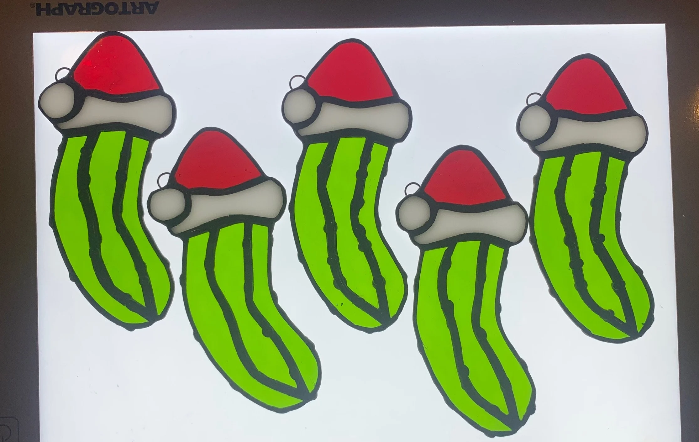 A stained glass panel featuring multiple green cacti with red and white Santa hats