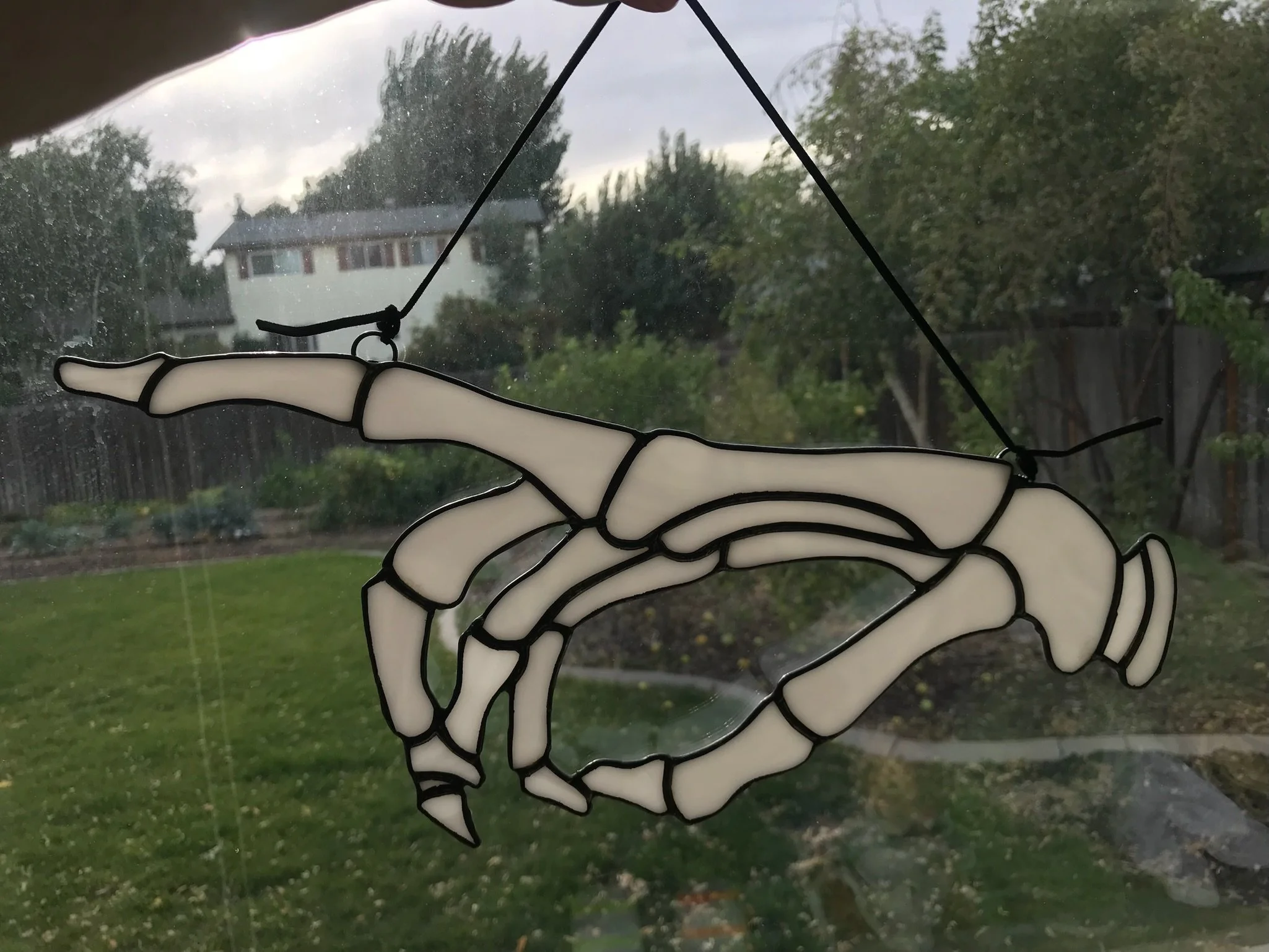 Decorative skeleton artwork hanging inside a house, with a window showing trees and a cloudy sky outside.