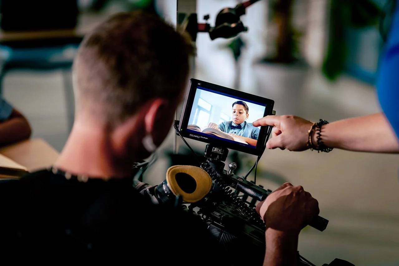Een persoon die achter een camera zit, film een jongen die leest en die te zien is op het scherm van de camera.