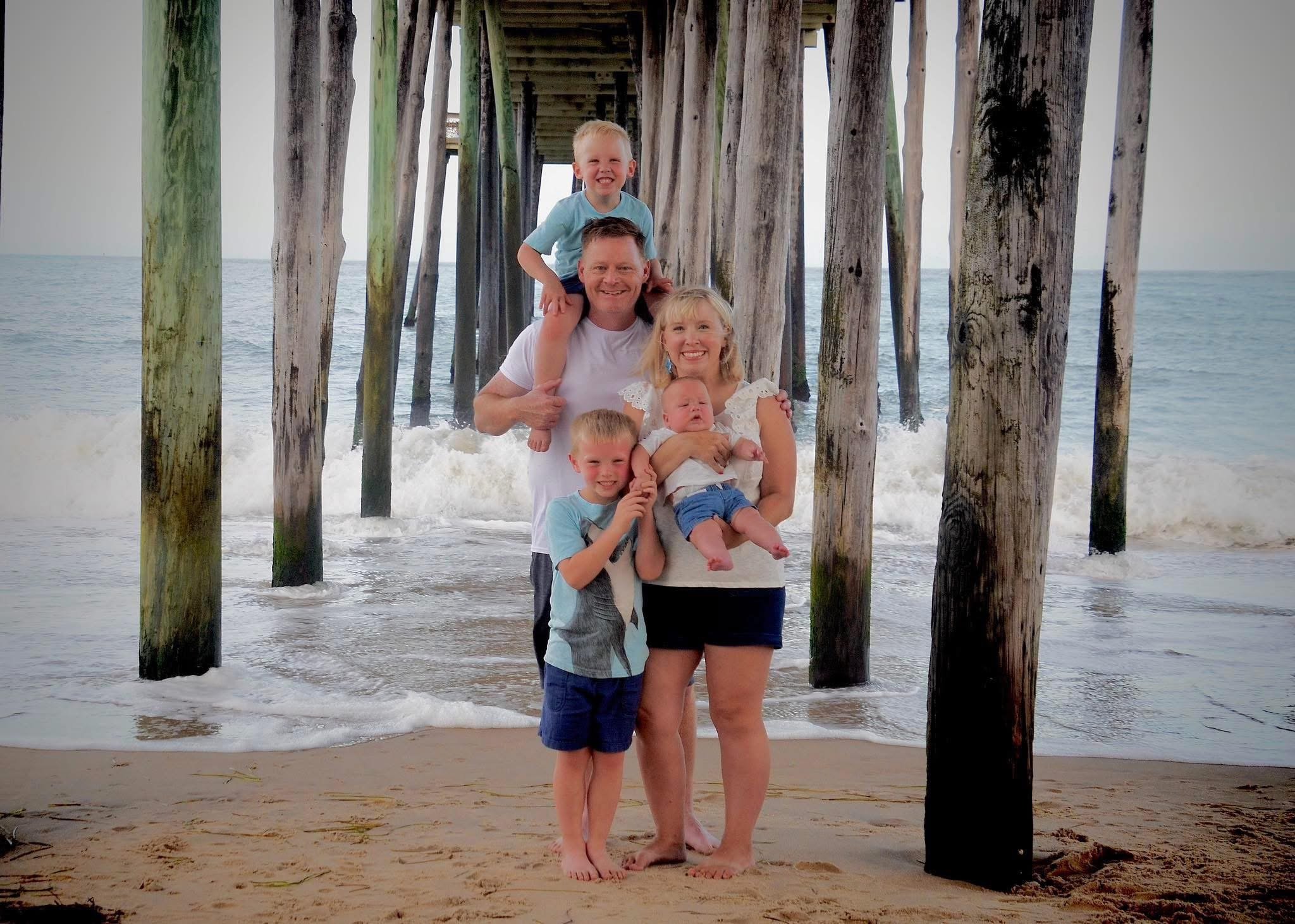 A family standing on a beach under a pier, smiling and enjoying the ocean view.