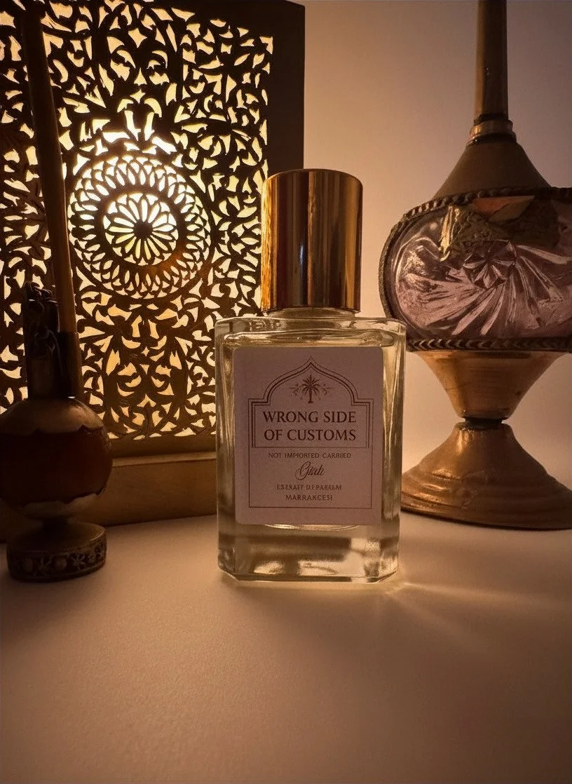 A perfume bottle labeled 'Wrong Side of Customs' in front of decorative items and a lit patterned lamp.