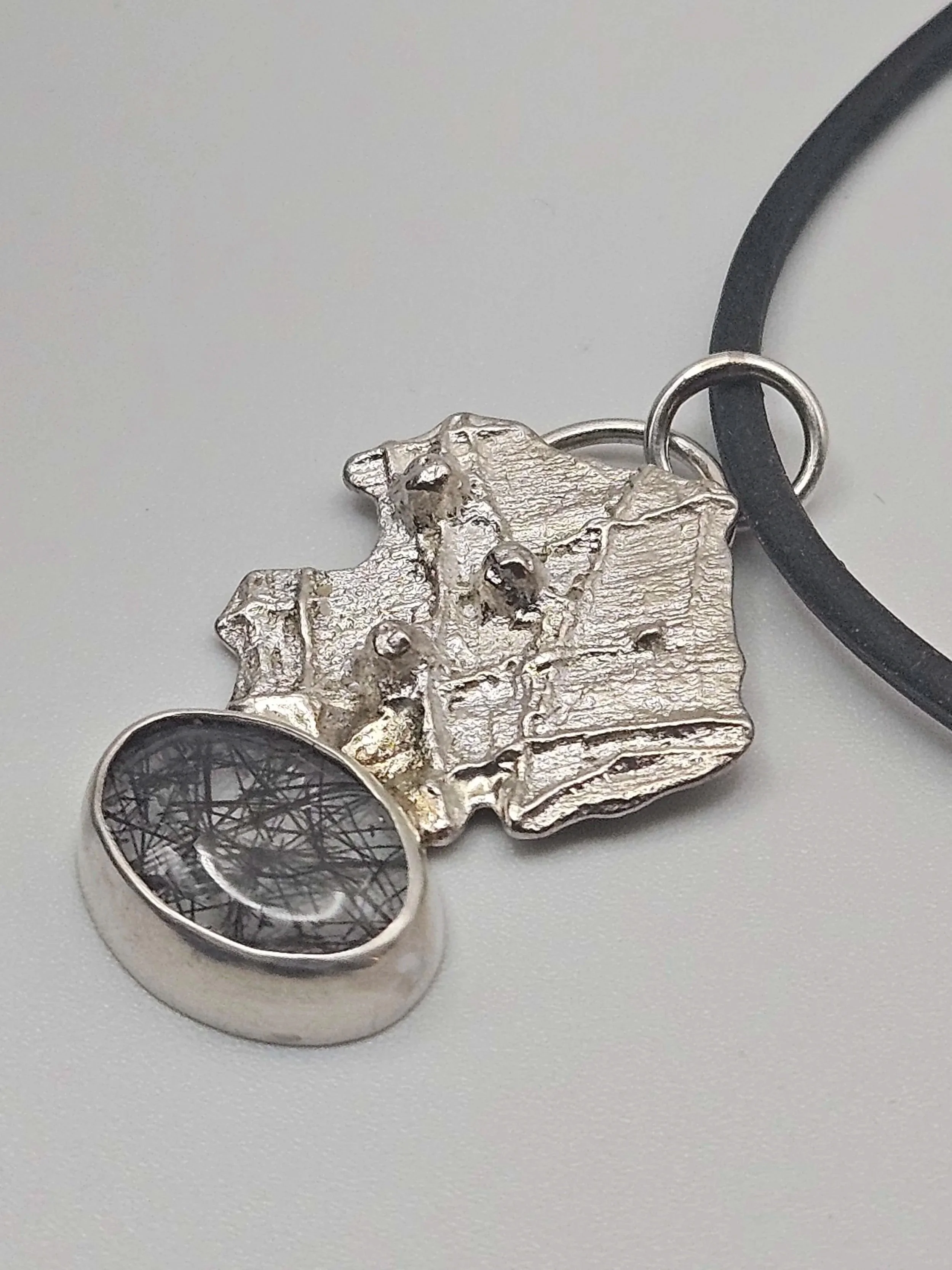 A silver pendant shaped like the state of California with embedded black stones, attached to a black leather cord.
