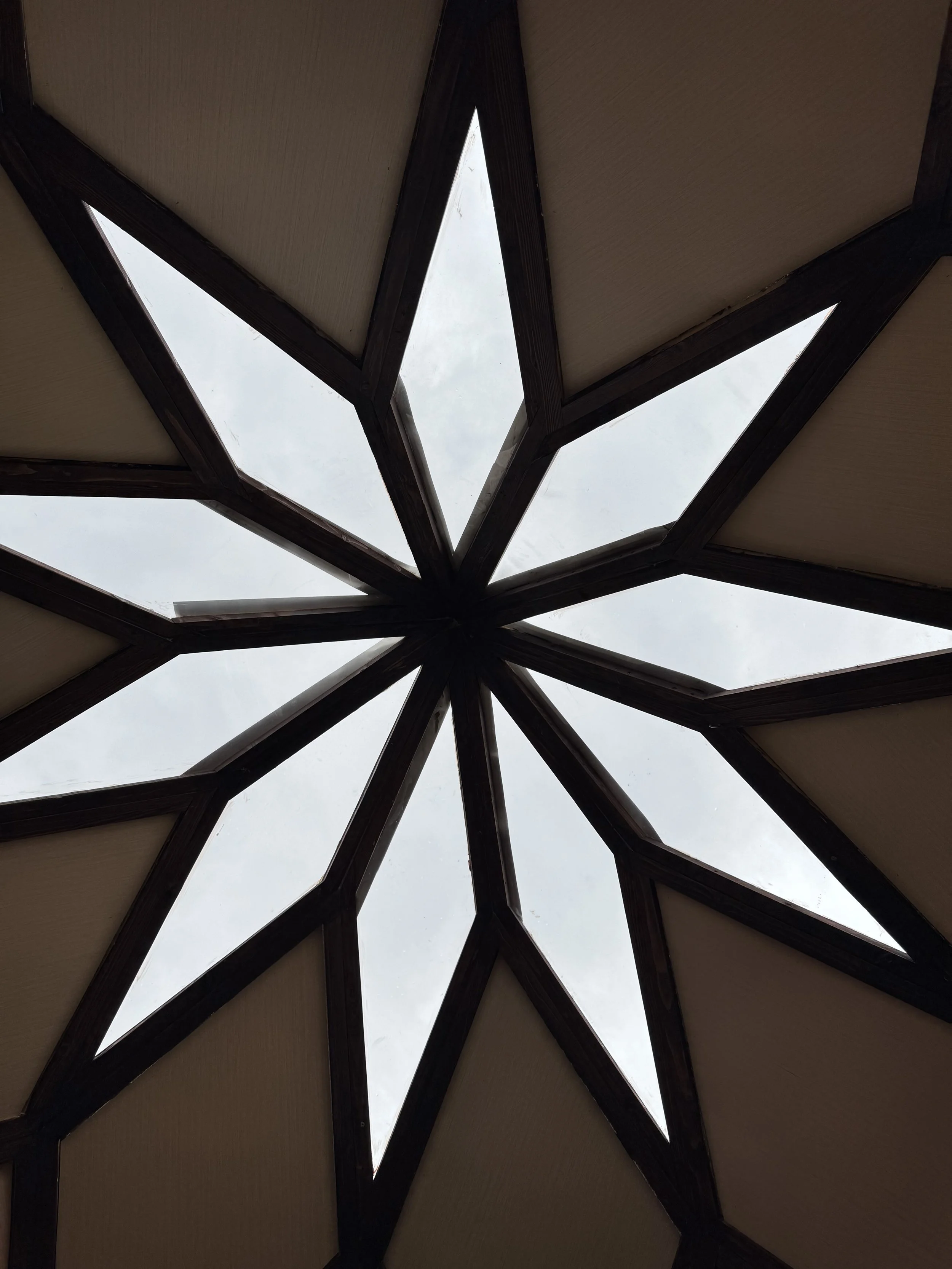 Looking up at a star-shaped skylight with wooden framing and glass panels.