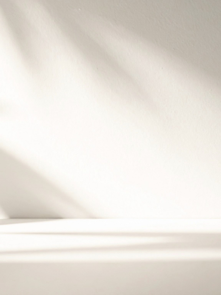 Close-up of a white surface with soft shadows and a smooth, textured wall in the background.