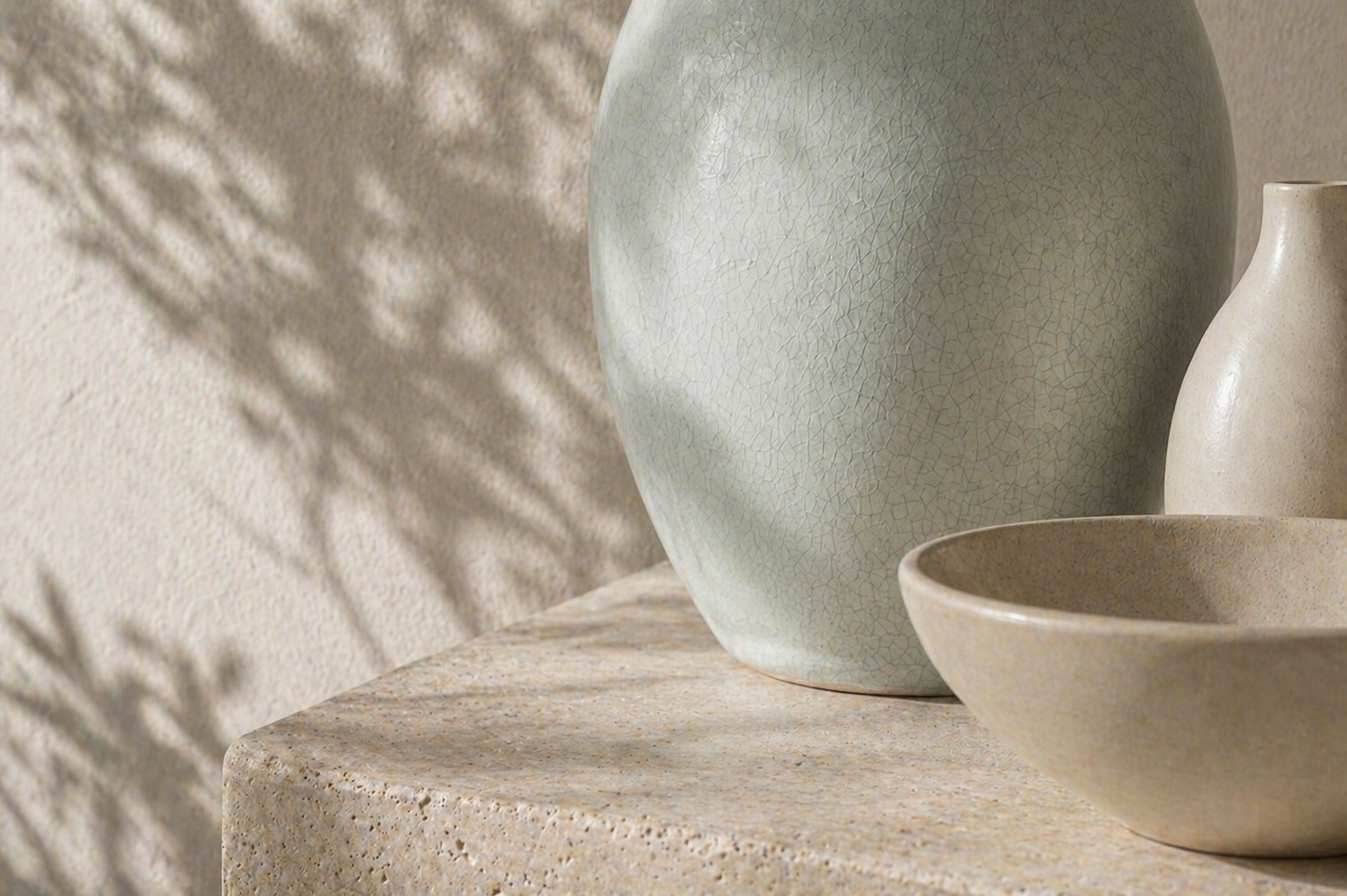 Close-up of ceramic vases and bowls on a textured surface with shadows cast on a wall.