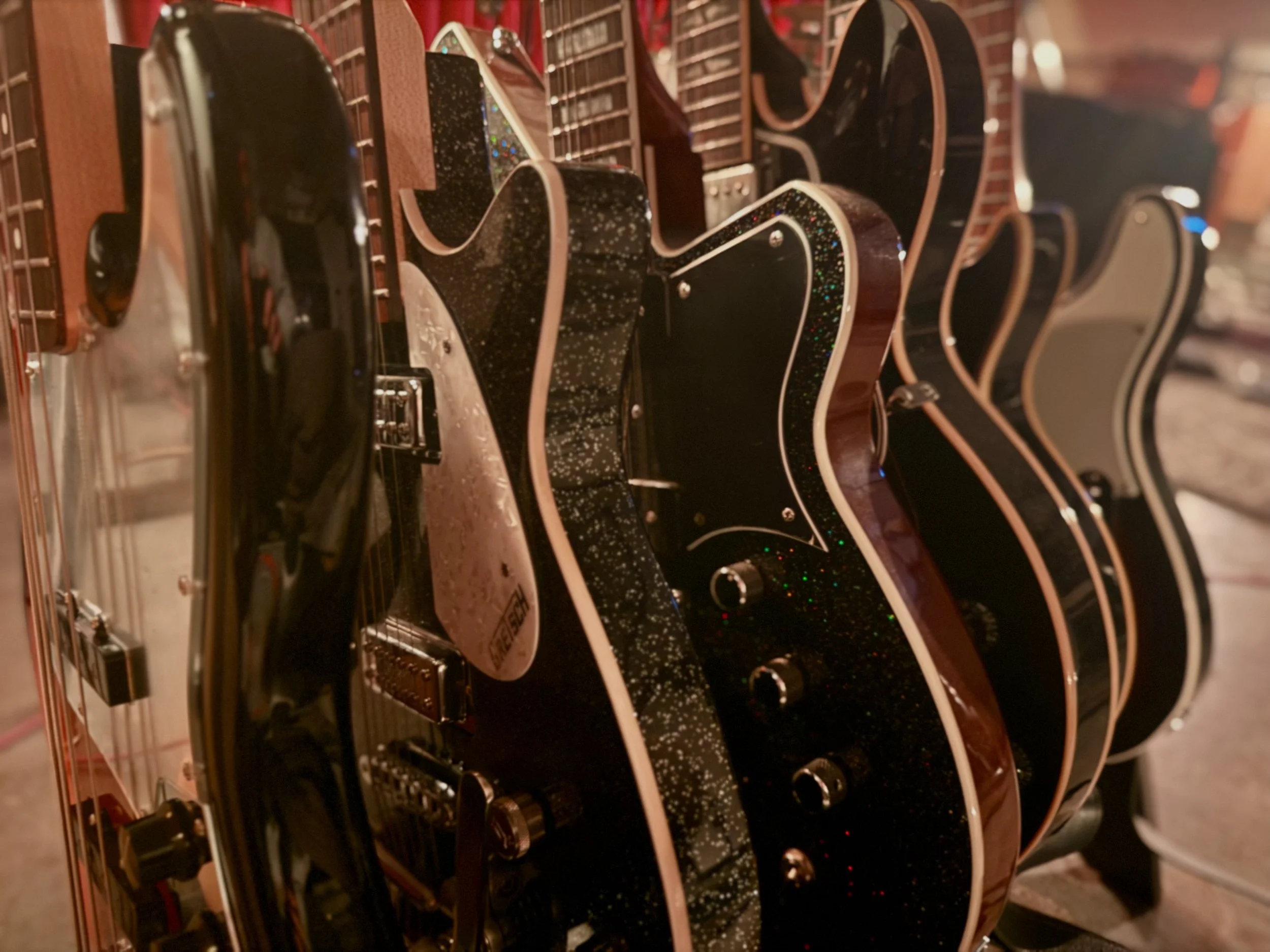 Several electric guitars with various finishes, including black, glittery black, and natural wood, hanging on a display rack in a music store.