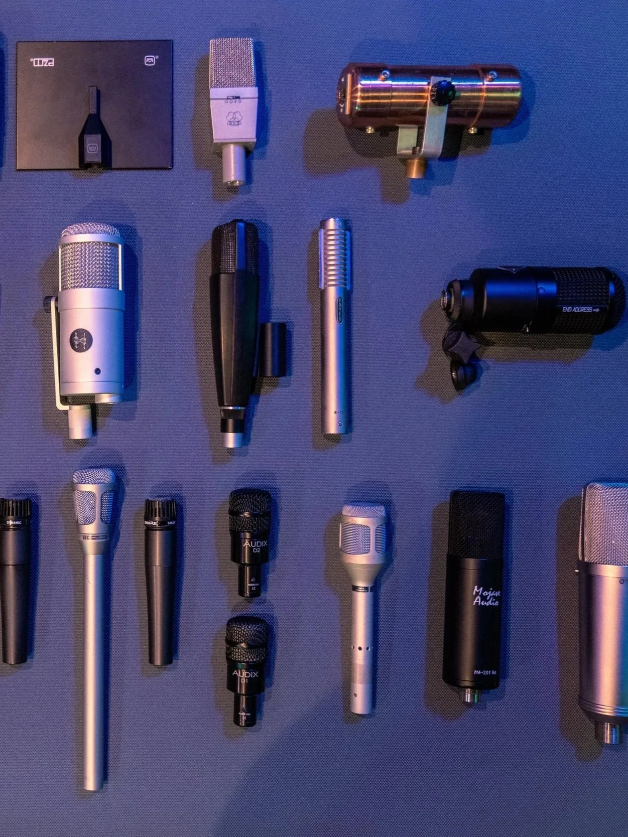 Collection of various professional microphones and microphone accessories arranged on a blue surface.