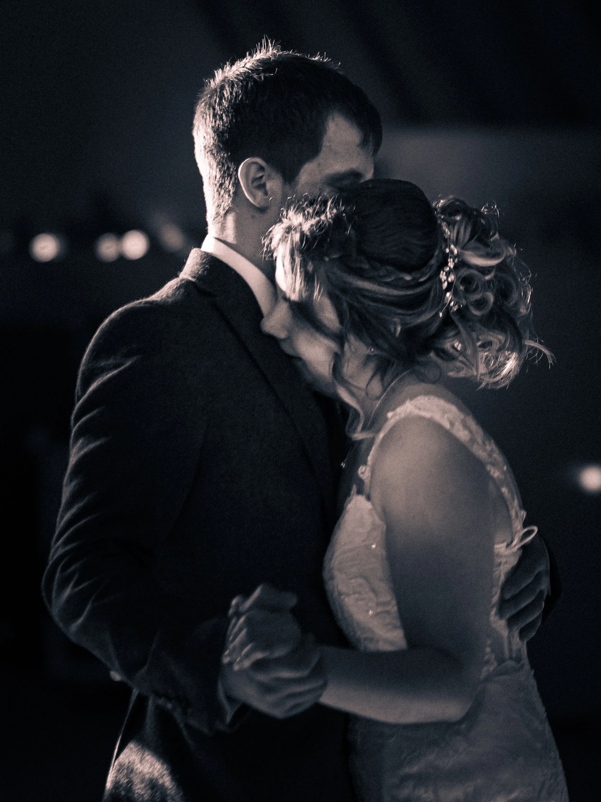 Black and white photo of a couple dancing closely, the man in a dark suit and the woman in a lace dress, embracing each other romantically.