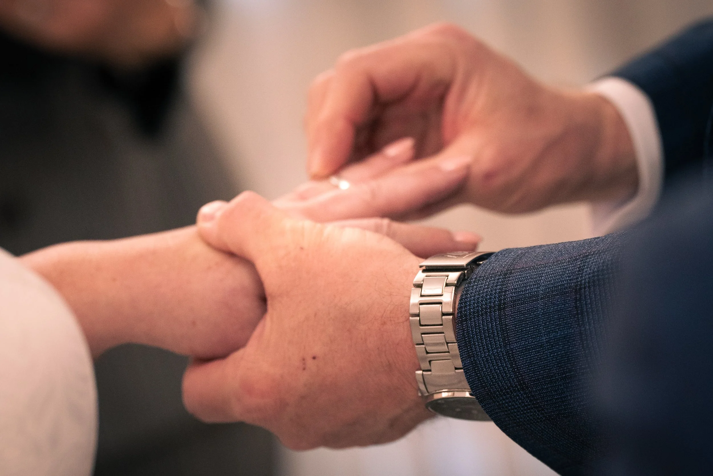 A man and a woman hold hands during a wedding ceremony, with the man's hand wearing a watch and the woman’s hand having a ring.