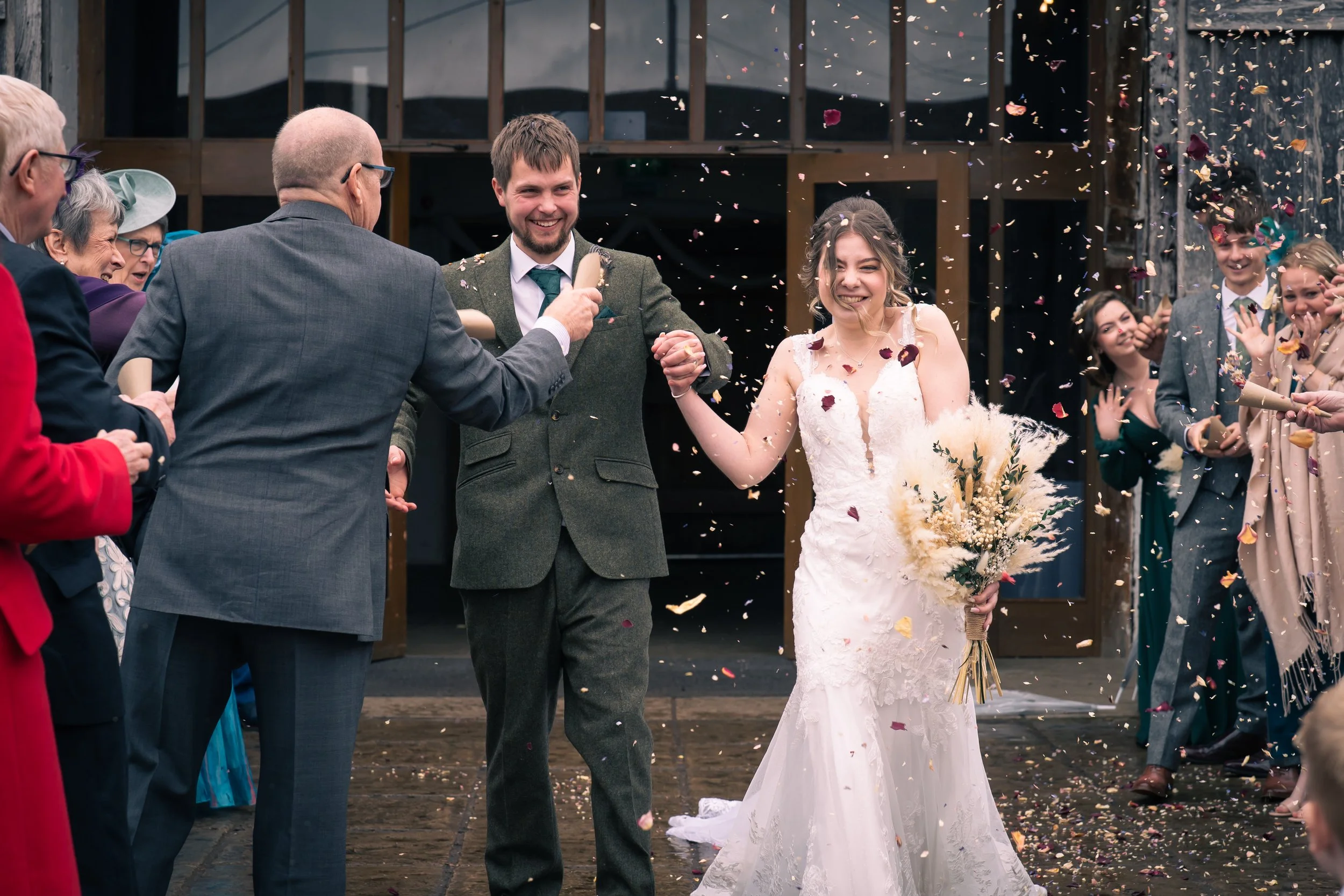 A bride and groom celebrate their wedding with friends and family, throwing confetti outside a building.