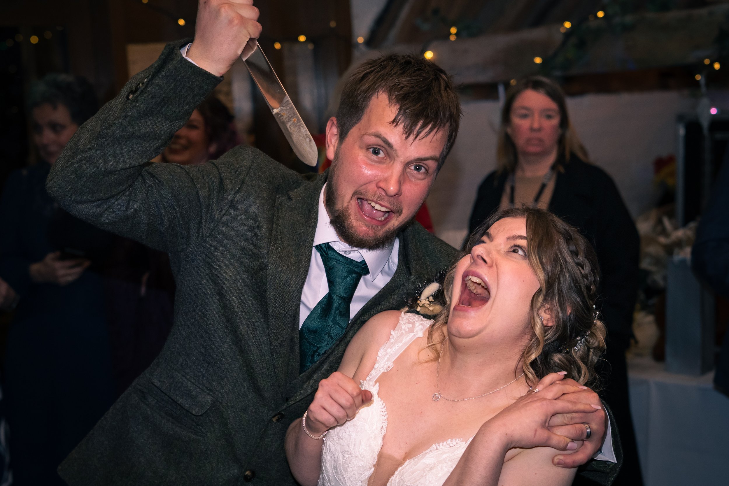 A man and woman celebrating at a wedding reception, with the man holding a knife and both of them laughing excitedly.