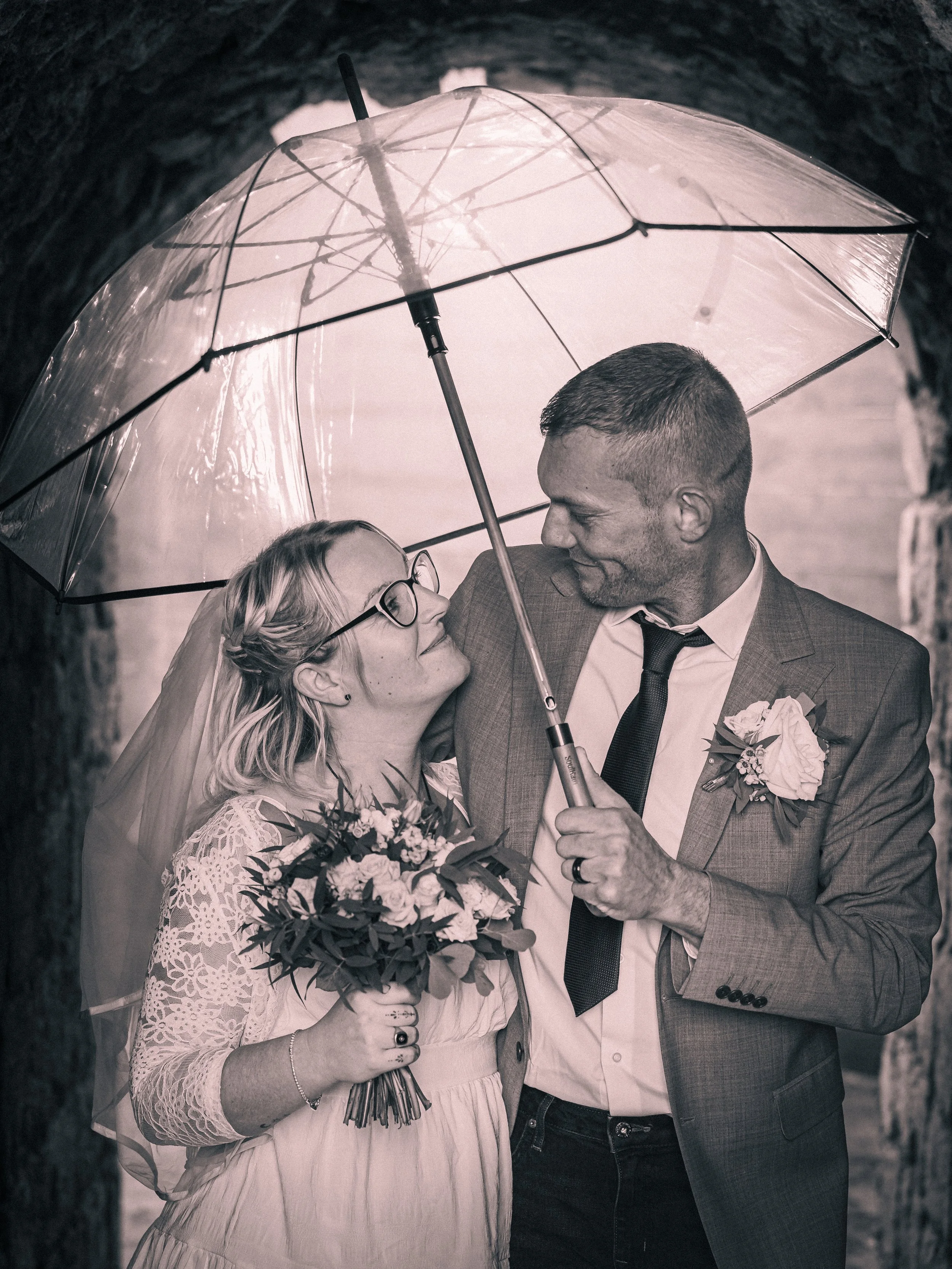 A bride and groom sharing a romantic moment under an umbrella during their wedding ceremony.