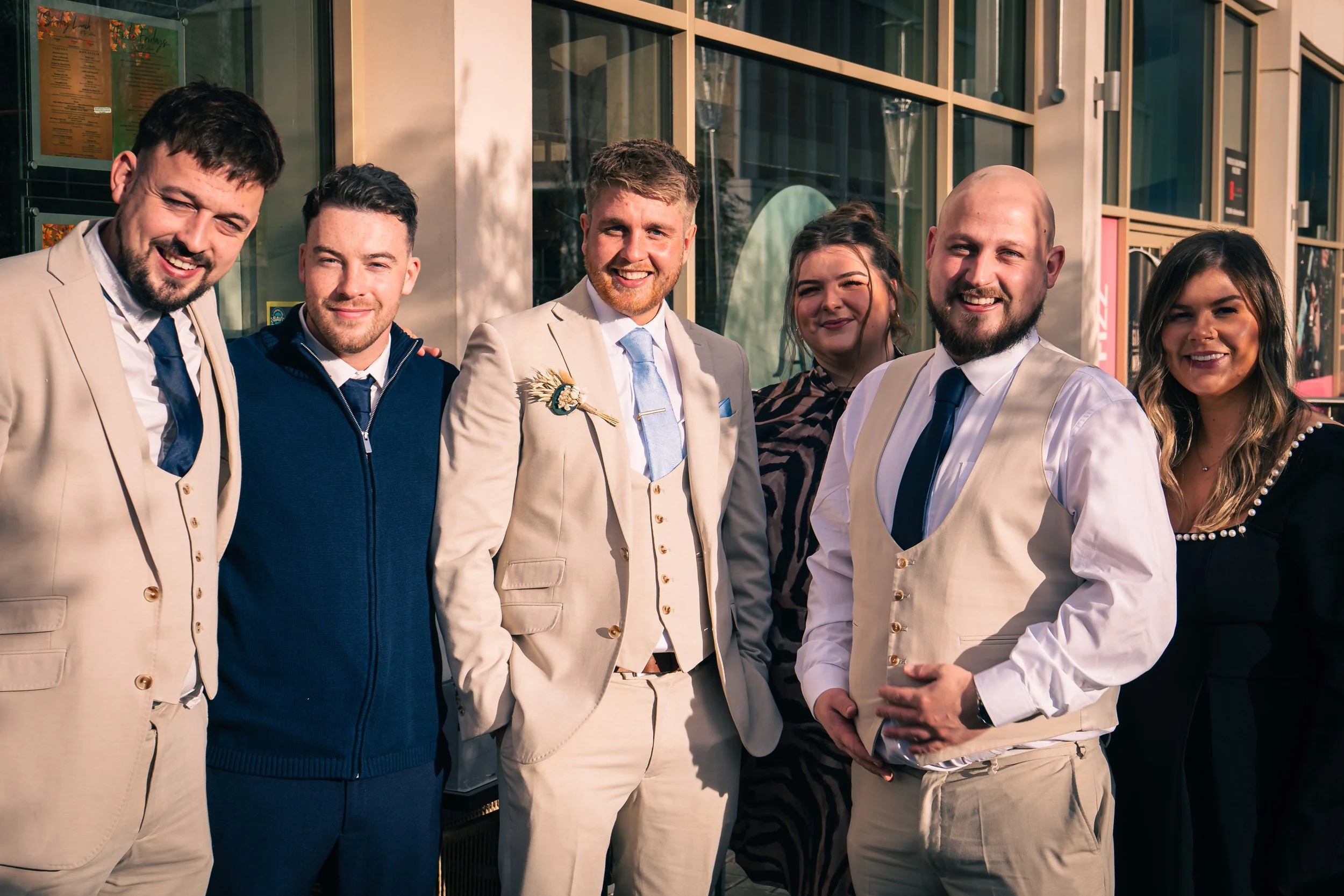 Group of seven smiling people standing outdoors on a sunny day