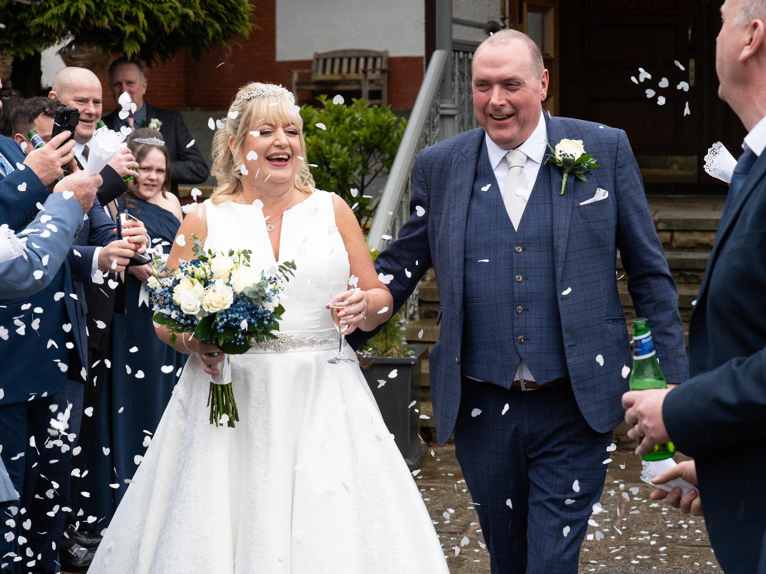 Bride and groom smiling as confetti is thrown during wedding celebration outside.