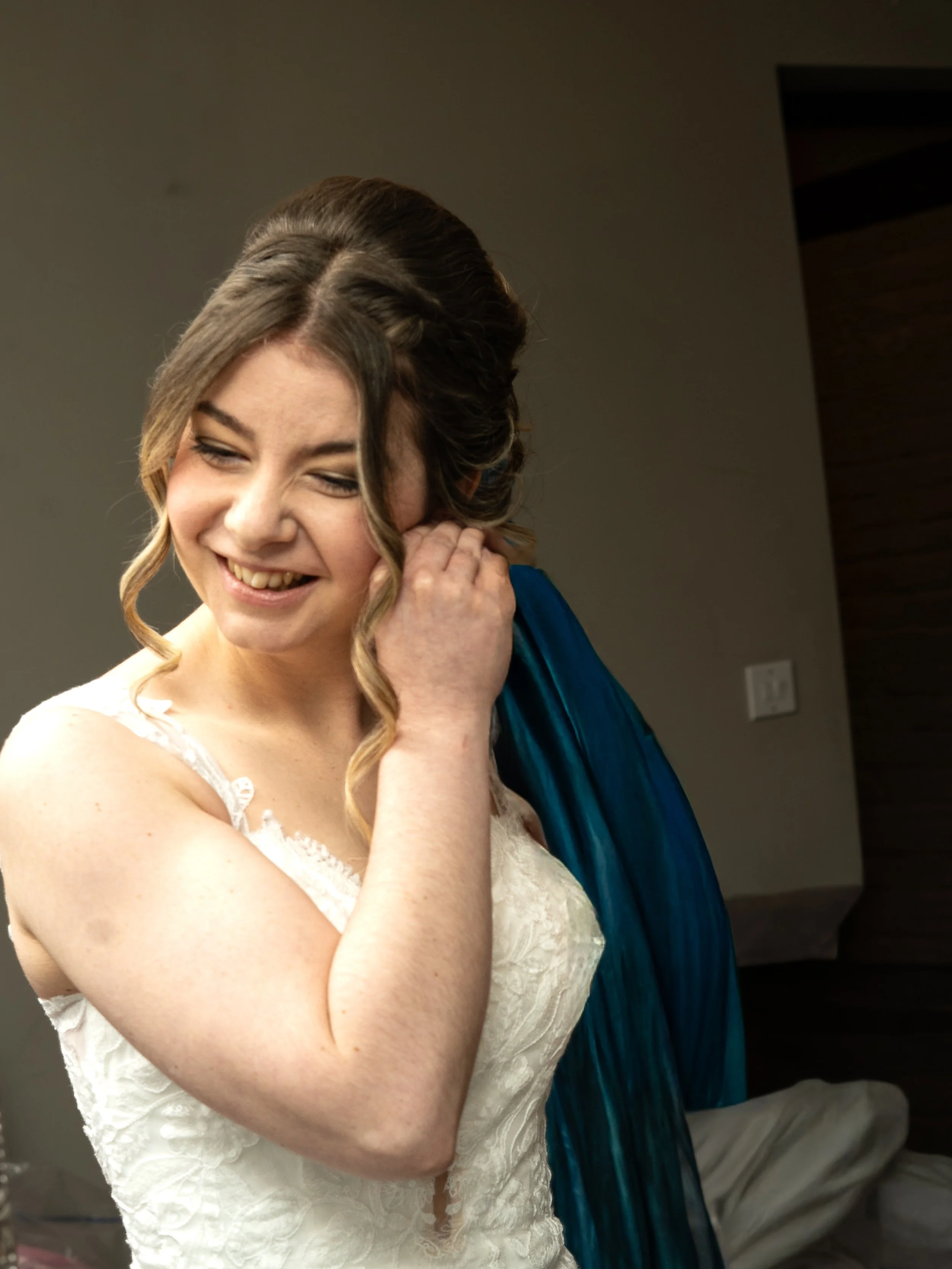 Bridal woman in a lace dress adjusting her hair with a smile.
