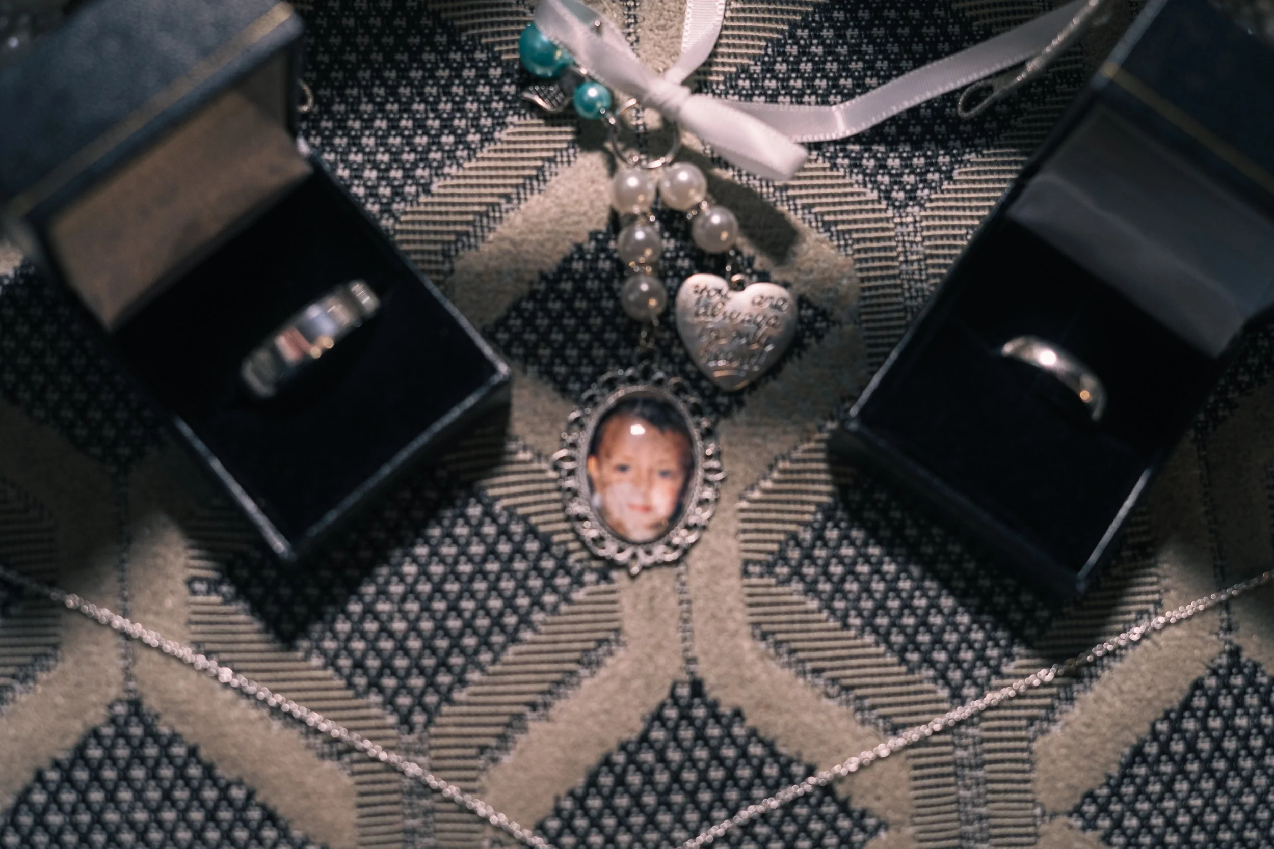 Various jewelry items including rings, a pearl necklace, and a pendant with a child’s photo on a patterned fabric surface.