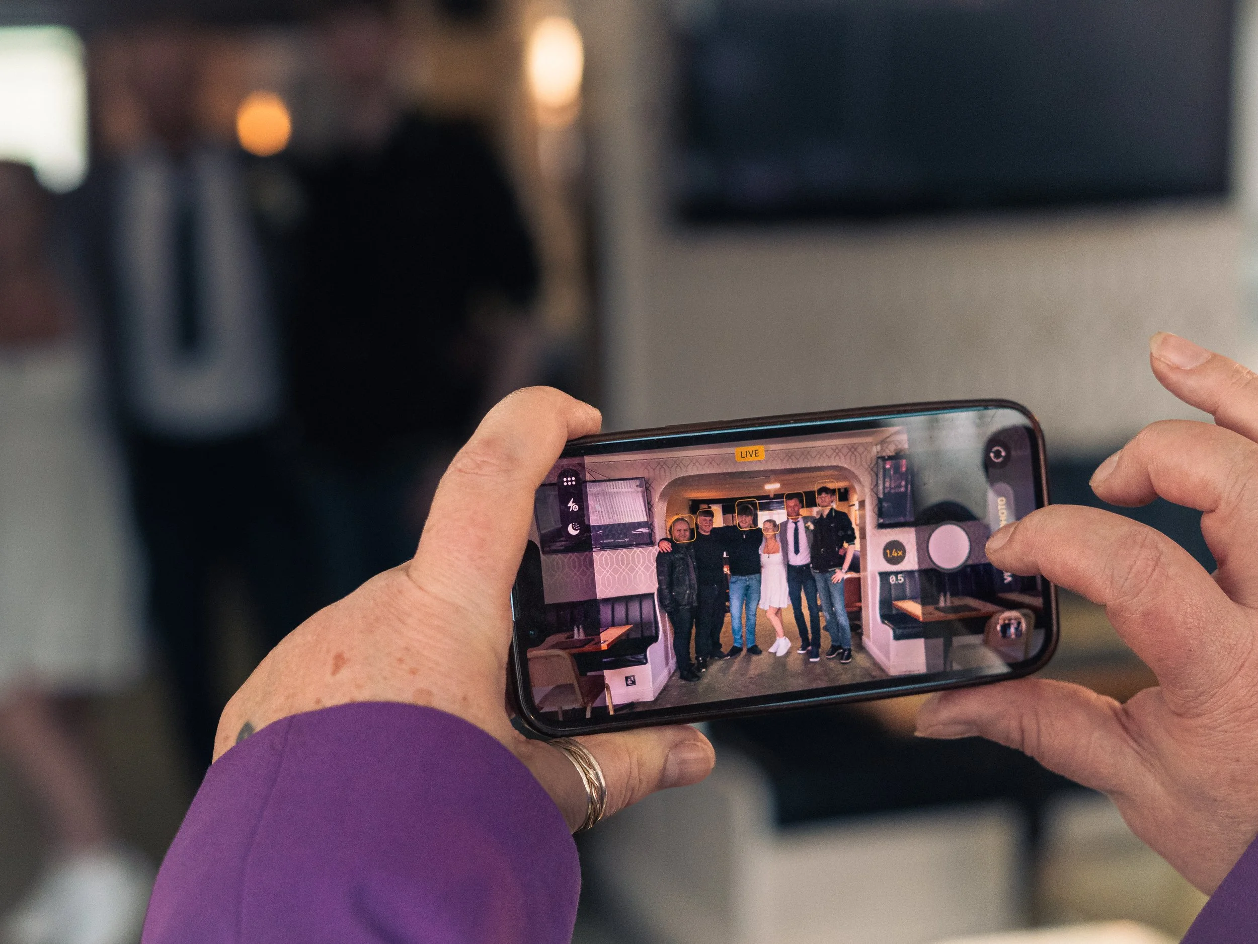 Person taking a photo of a group of five people standing together inside a restaurant or cafe.