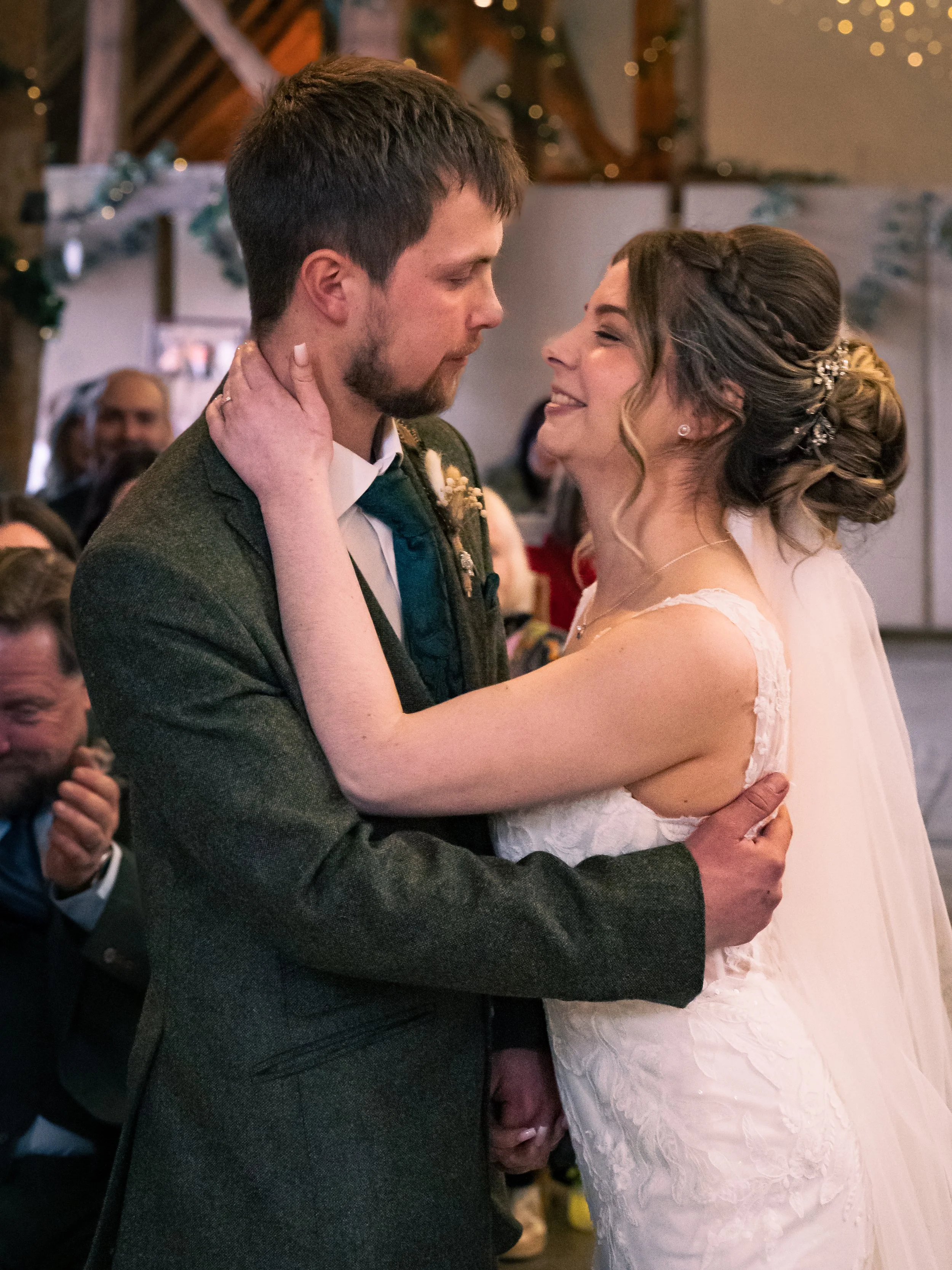 A bride and groom sharing a dance at their wedding reception, looking into each other's eyes and smiling, with guests in the background.