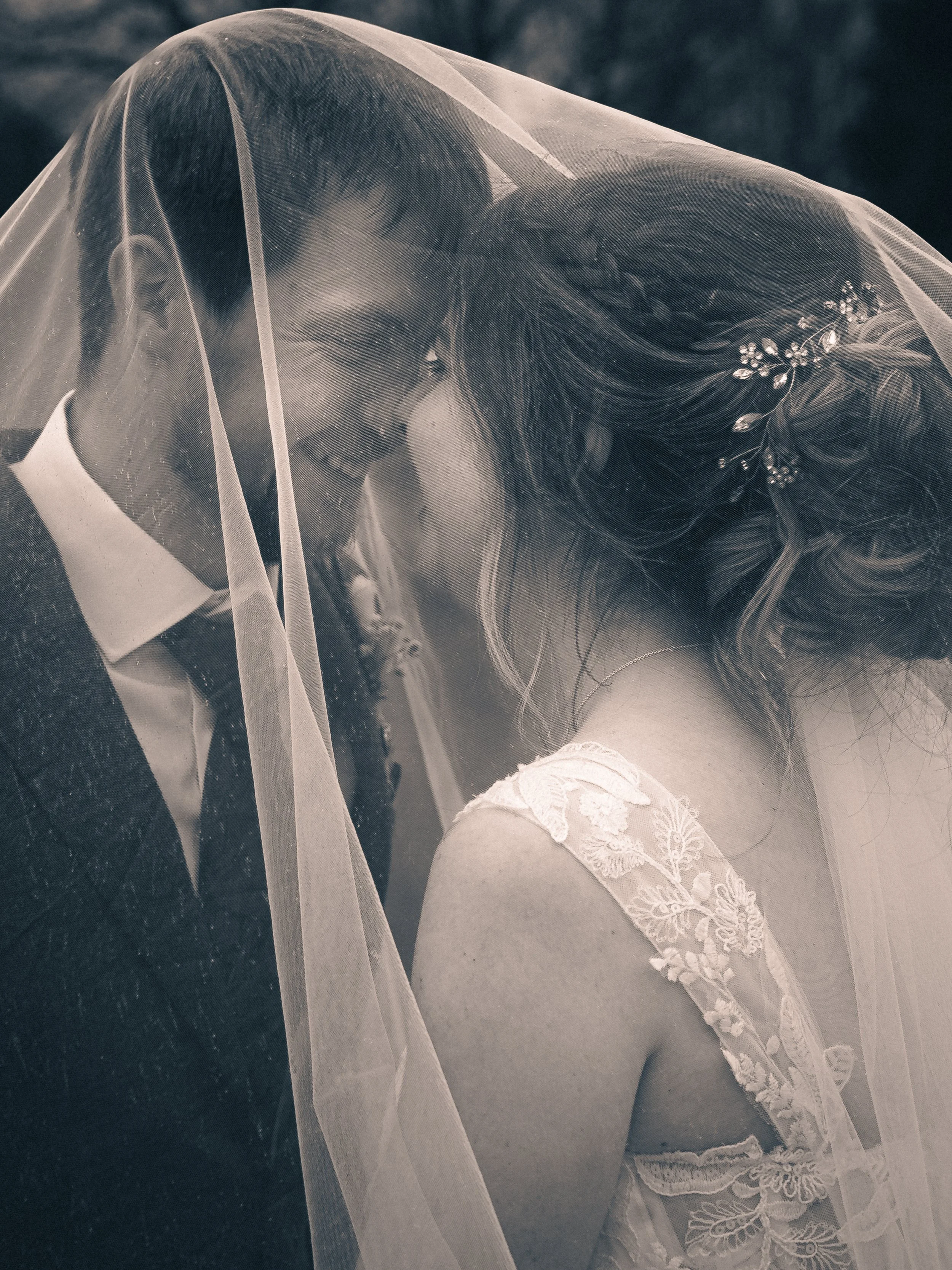Close-up of a bride and groom with their foreheads touching, under a veil, celebrating their wedding day.