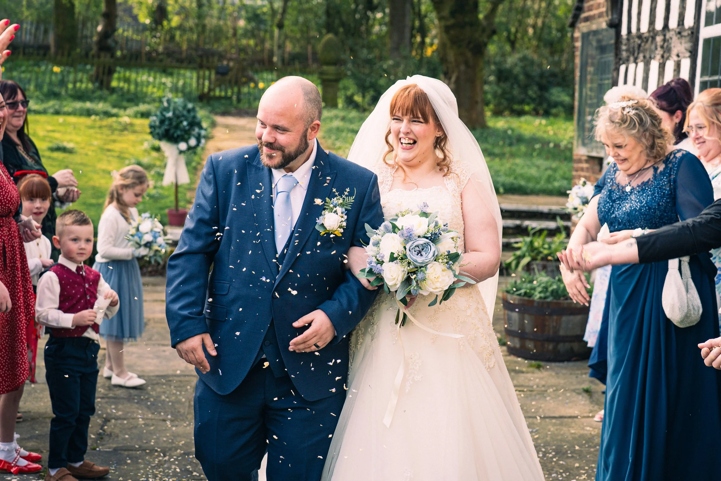 Bride and groom walking together at their wedding outdoor celebration, surrounded by friends and family, with confetti falling around them.
