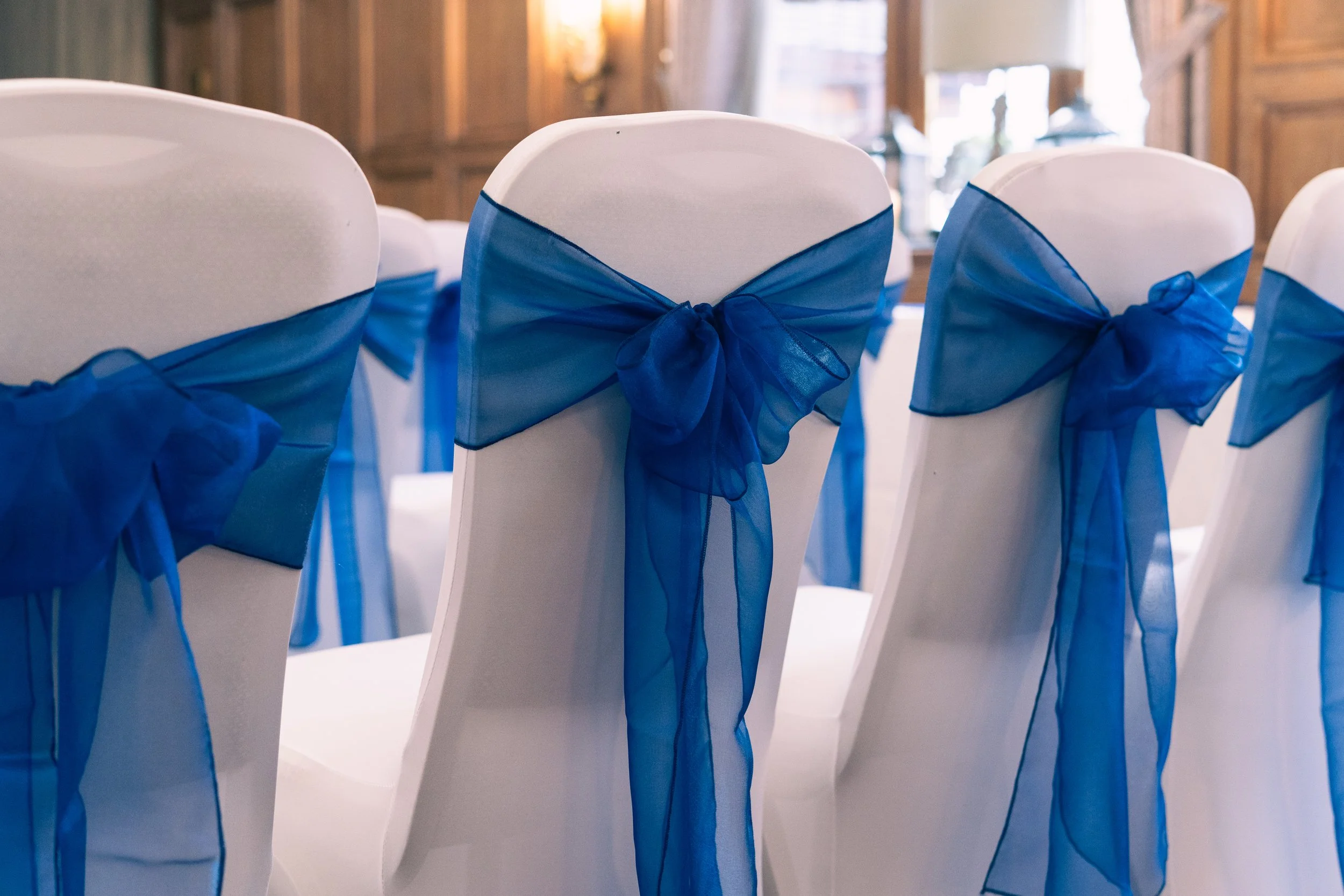 White chairs decorated with blue organza sashes tied in bows, arranged in a row for a wedding or event.