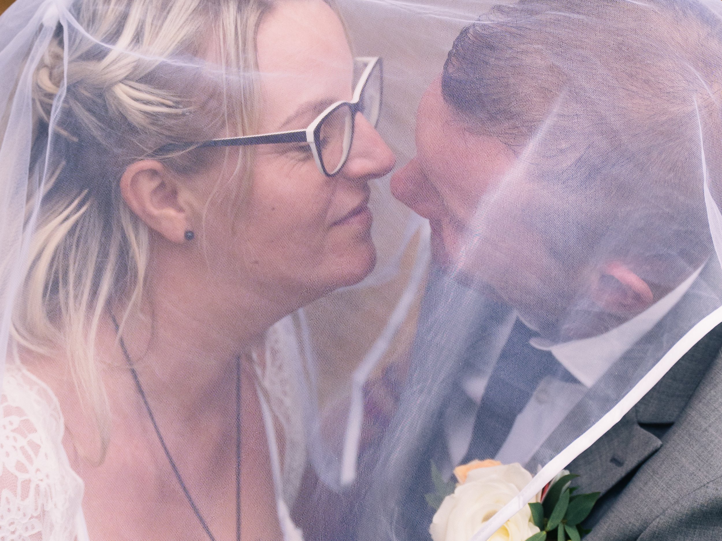 A bride and groom are close under a white veil during their wedding ceremony.
