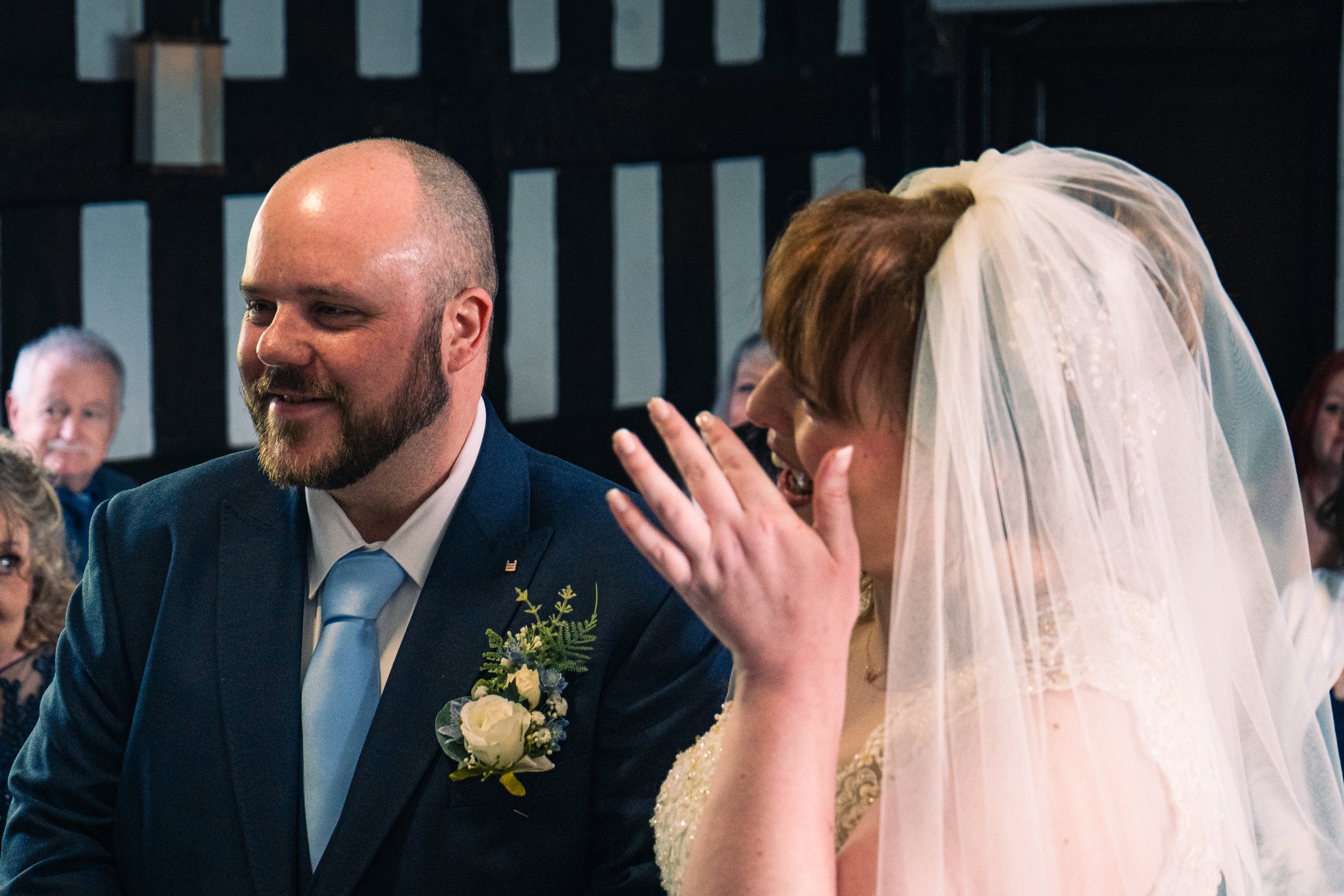 A wedding ceremony with a bride and groom smiling, surrounded by guests, indoors with dark wood walls.