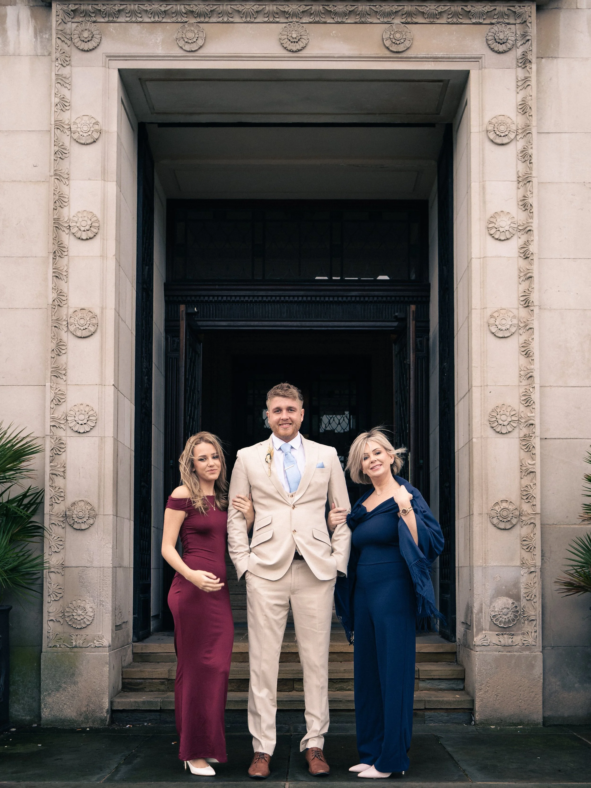 Group of three people standing on steps outside a building, dressed in formal attire.