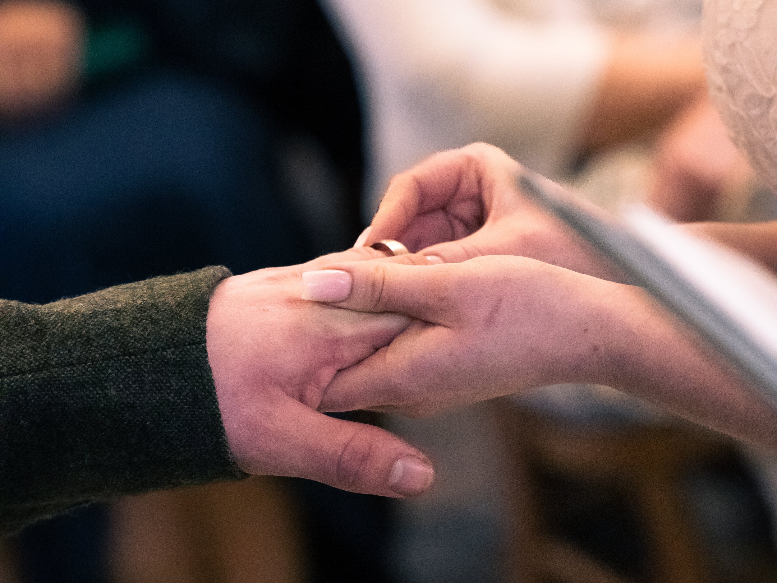 Two people holding hands gently, one with a beige long-sleeve shirt and the other with a darker long-sleeve shirt.