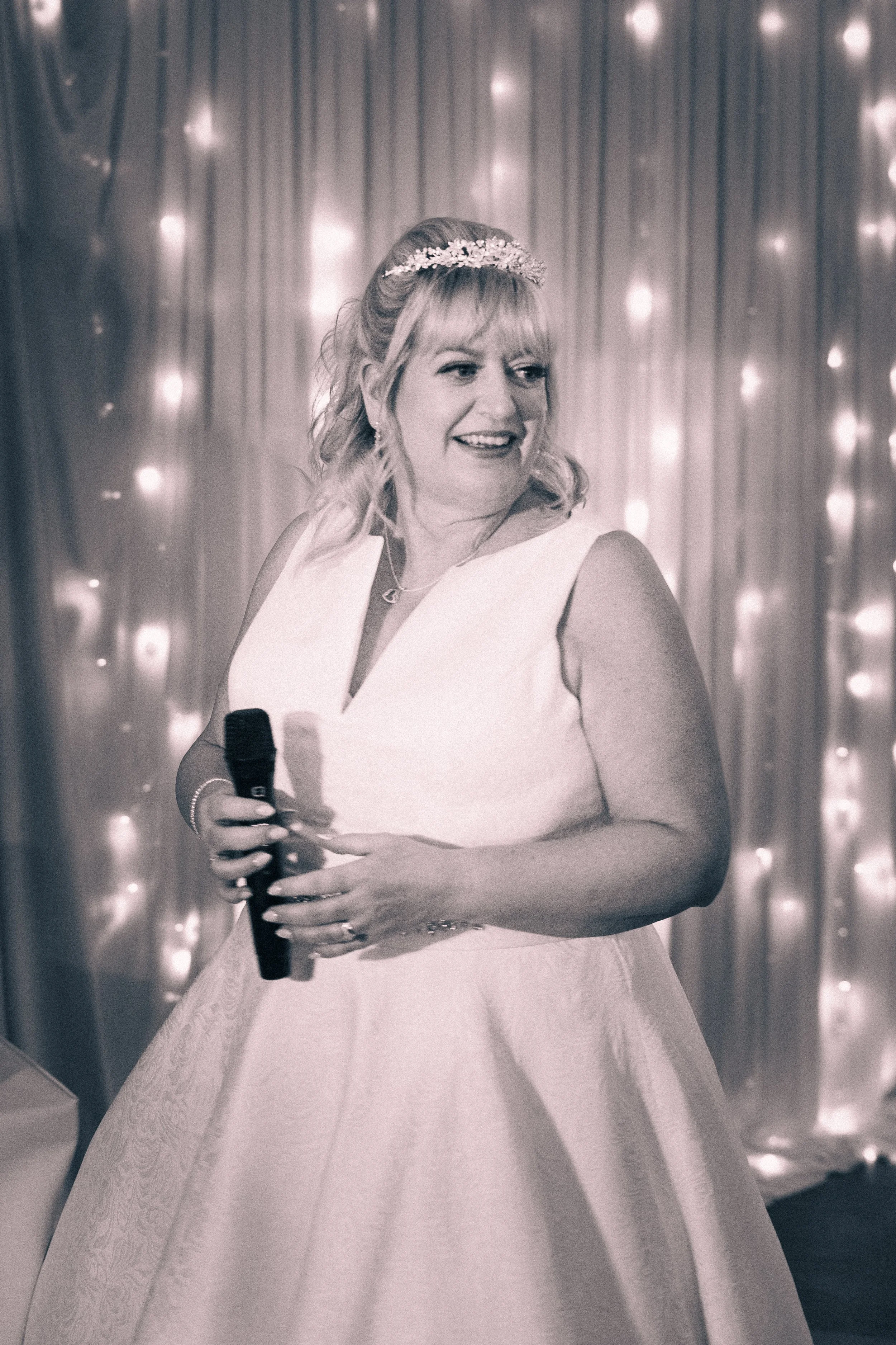 A woman in a wedding dress holding a microphone at wedding reception.