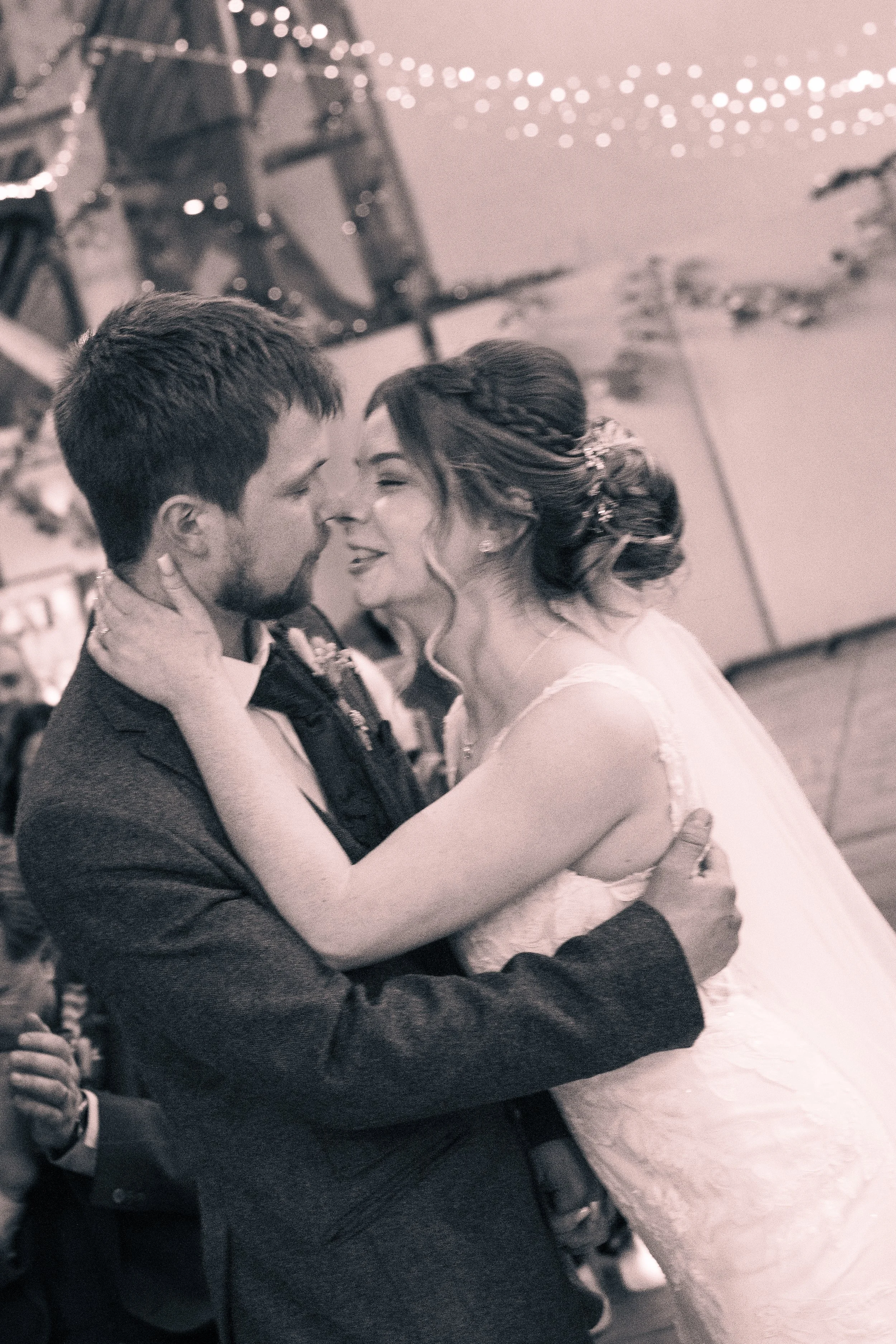 A couple in wedding attire sharing a dance at their wedding reception, with string lights and a dance floor in the background.