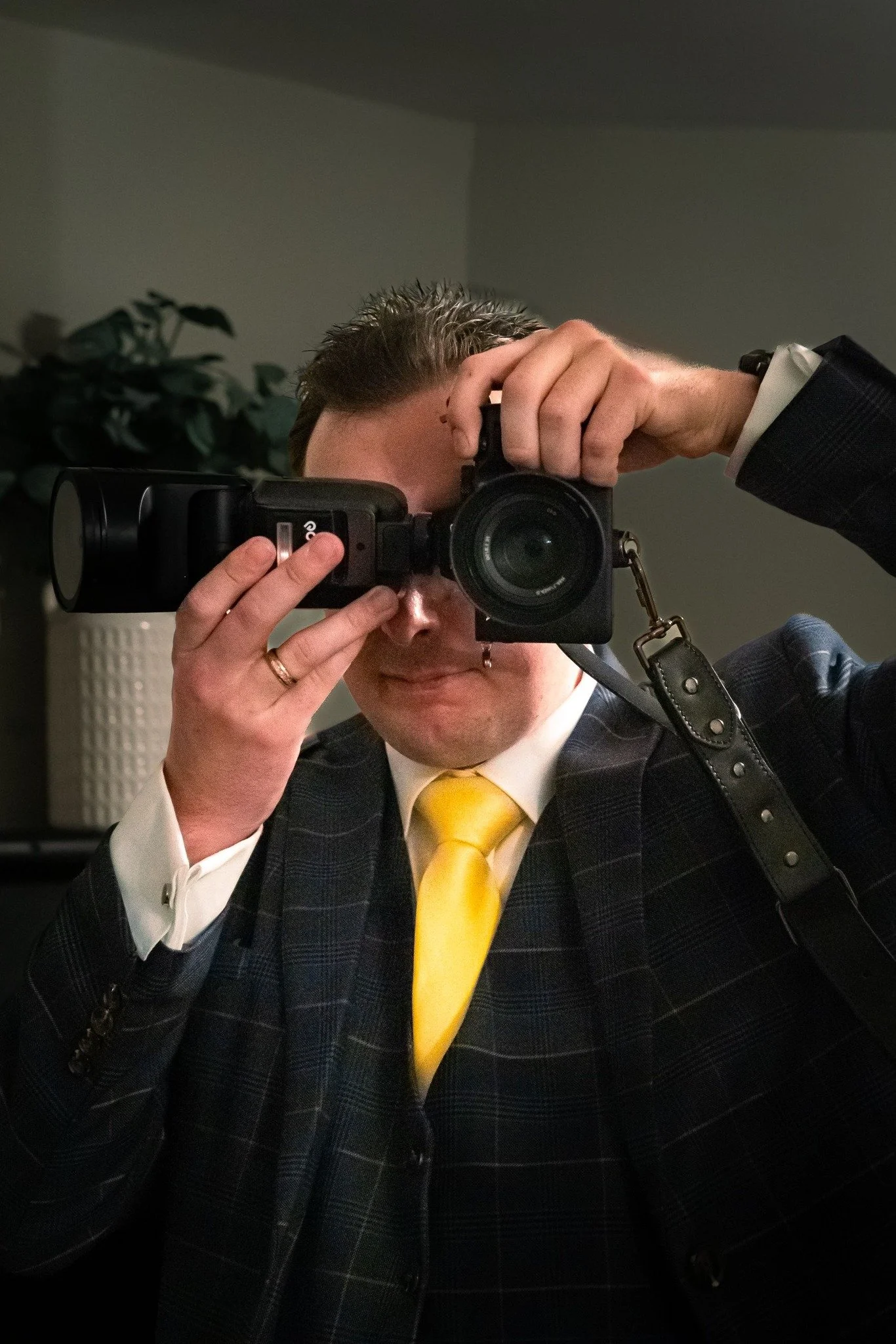 Person dressed in a suit with a yellow tie taking a selfie using a camera.