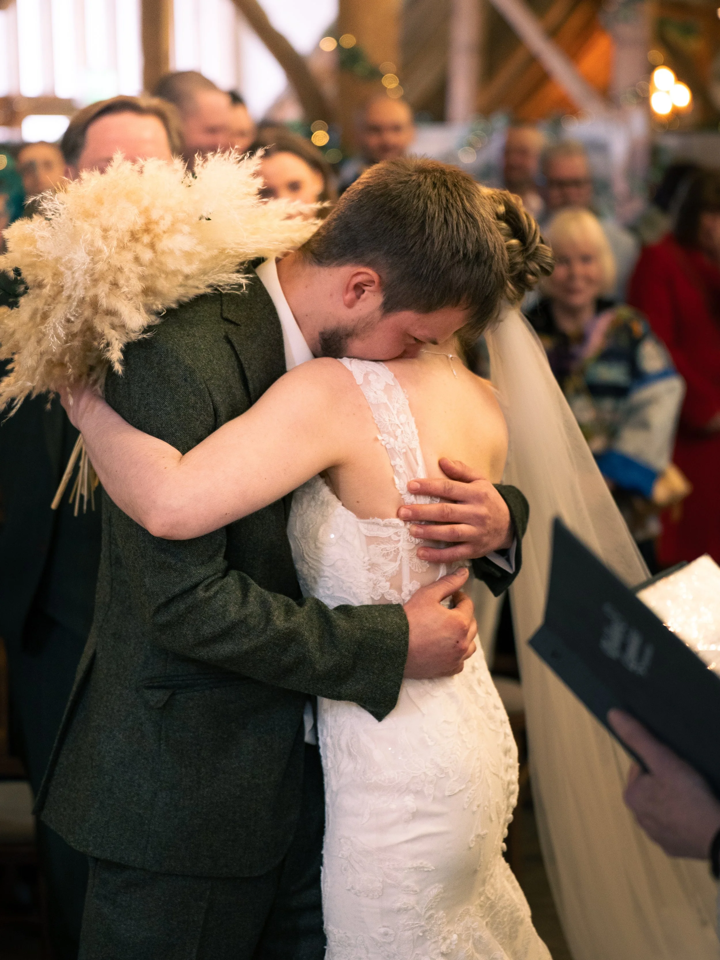 A couple embraces during a wedding ceremony, with guests in the background watching.