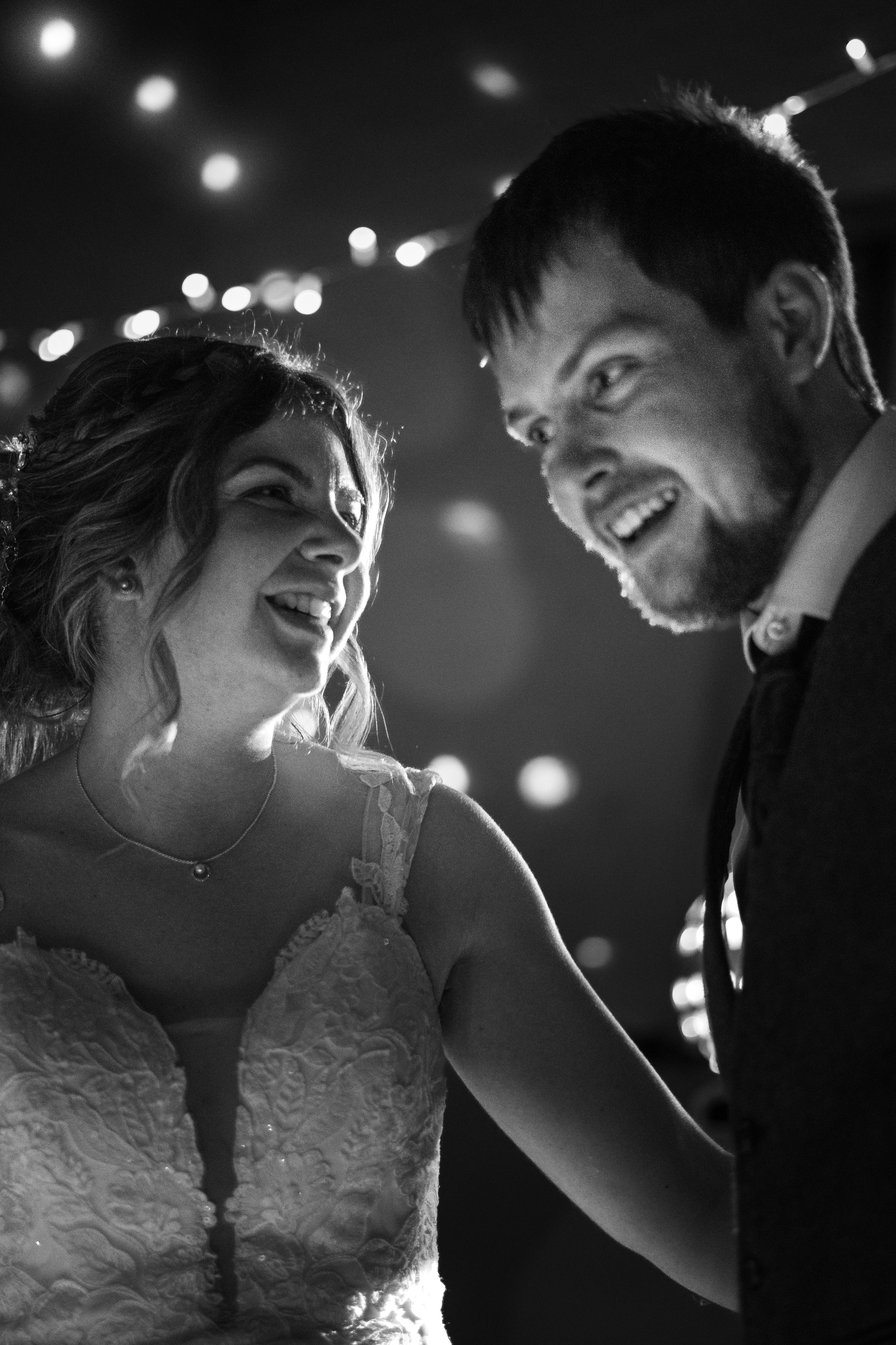 A black and white photo of a bride and groom smiling and dancing together at their wedding reception.
