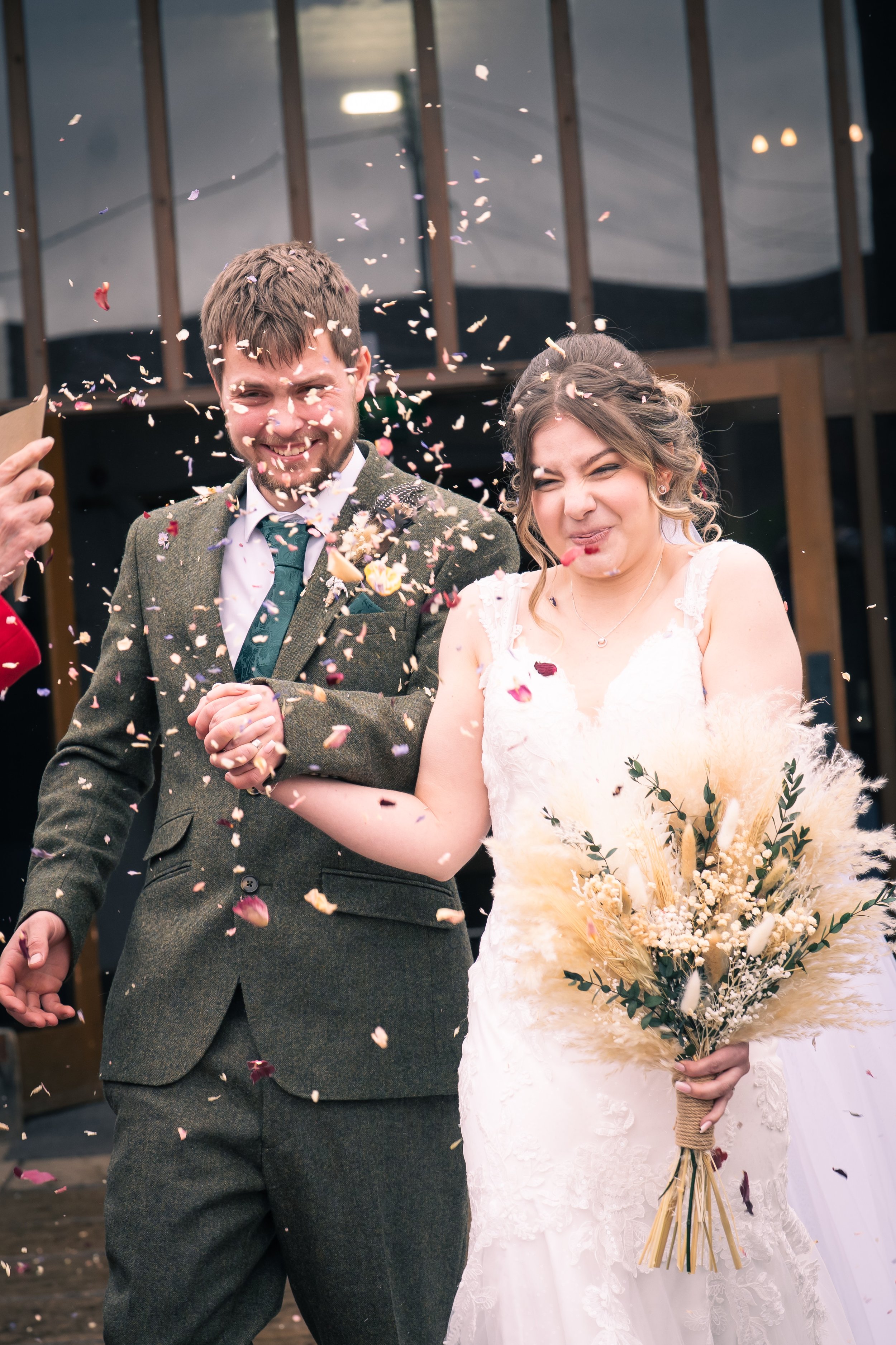 A bride and groom smiling and holding hands amid confetti at their wedding celebration.