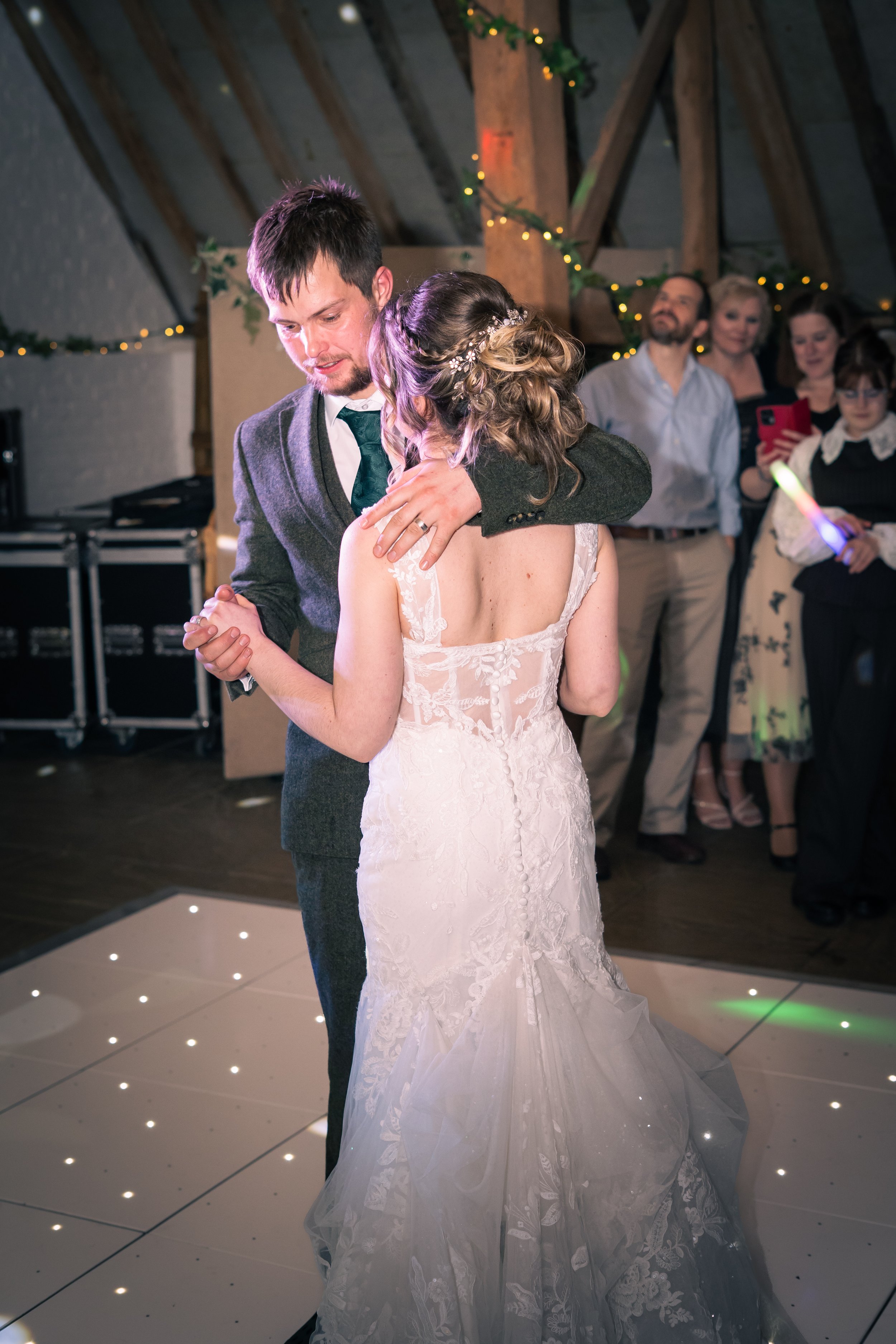 A bride and groom sharing their first dance at a wedding reception, with guests watching in the background.