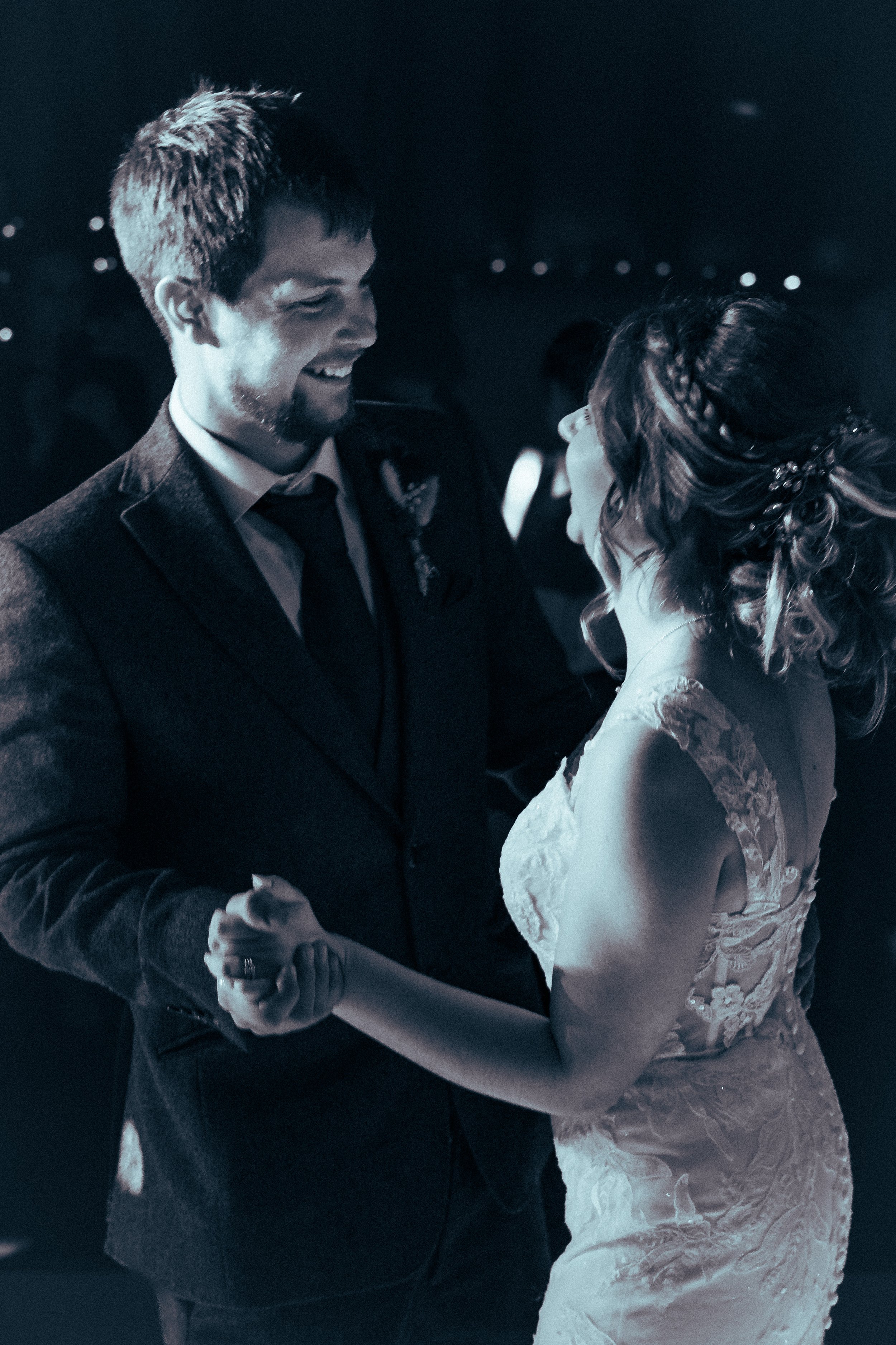 A man and woman dancing together at a formal event, with the woman wearing a lace dress and the man in a suit, smiling and looking at each other.