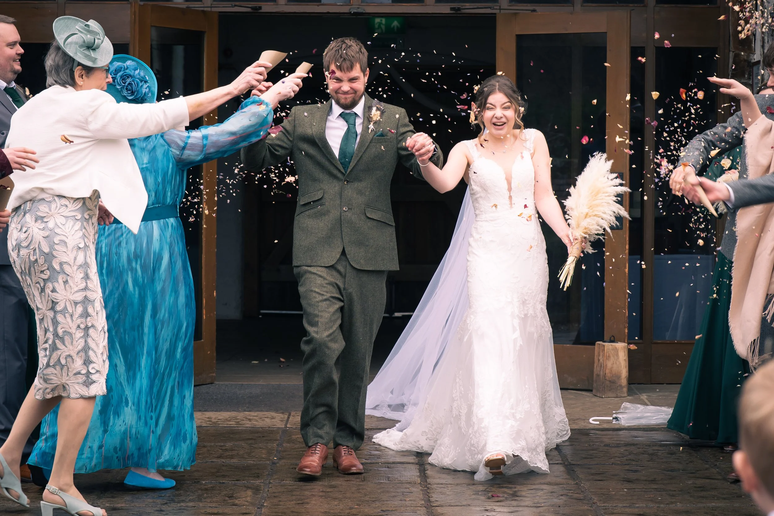 A bride and groom walking hand in hand, smiling, as they leave a wedding celebration amid confetti and guests on either side.