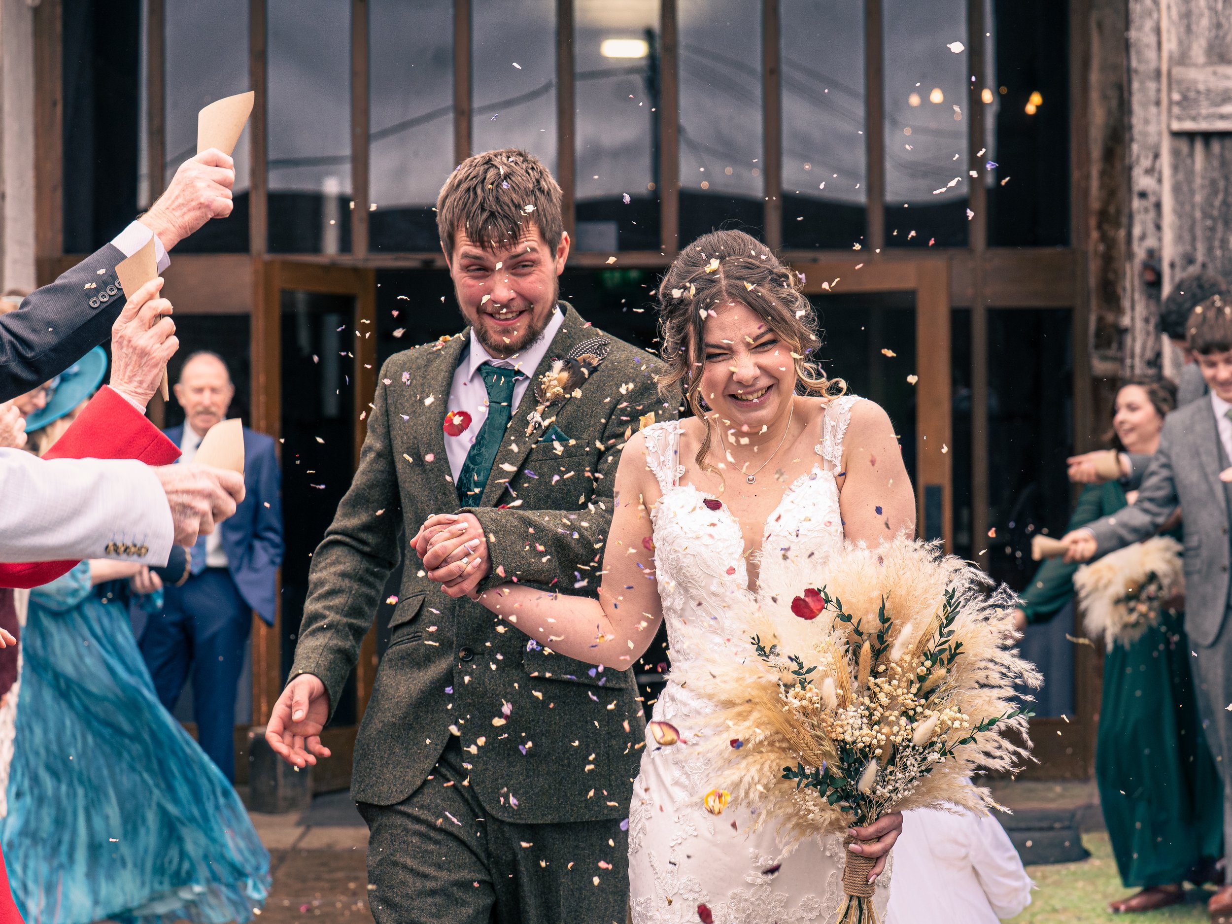 A bride and groom smiling and celebrating as they walk outside surrounded by guests throwing confetti.