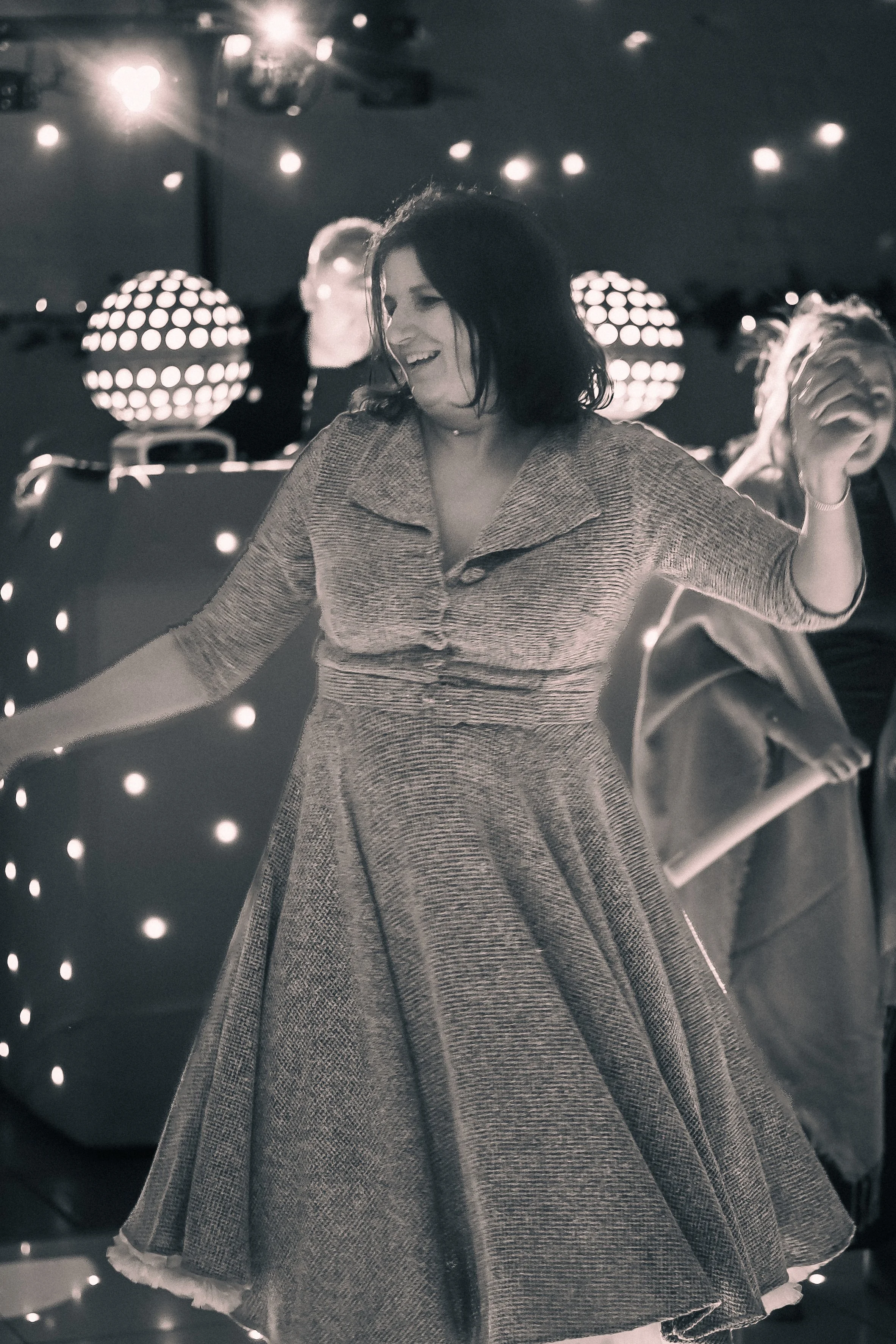 A woman dancing at a party with string lights and illuminated disco balls in the background.