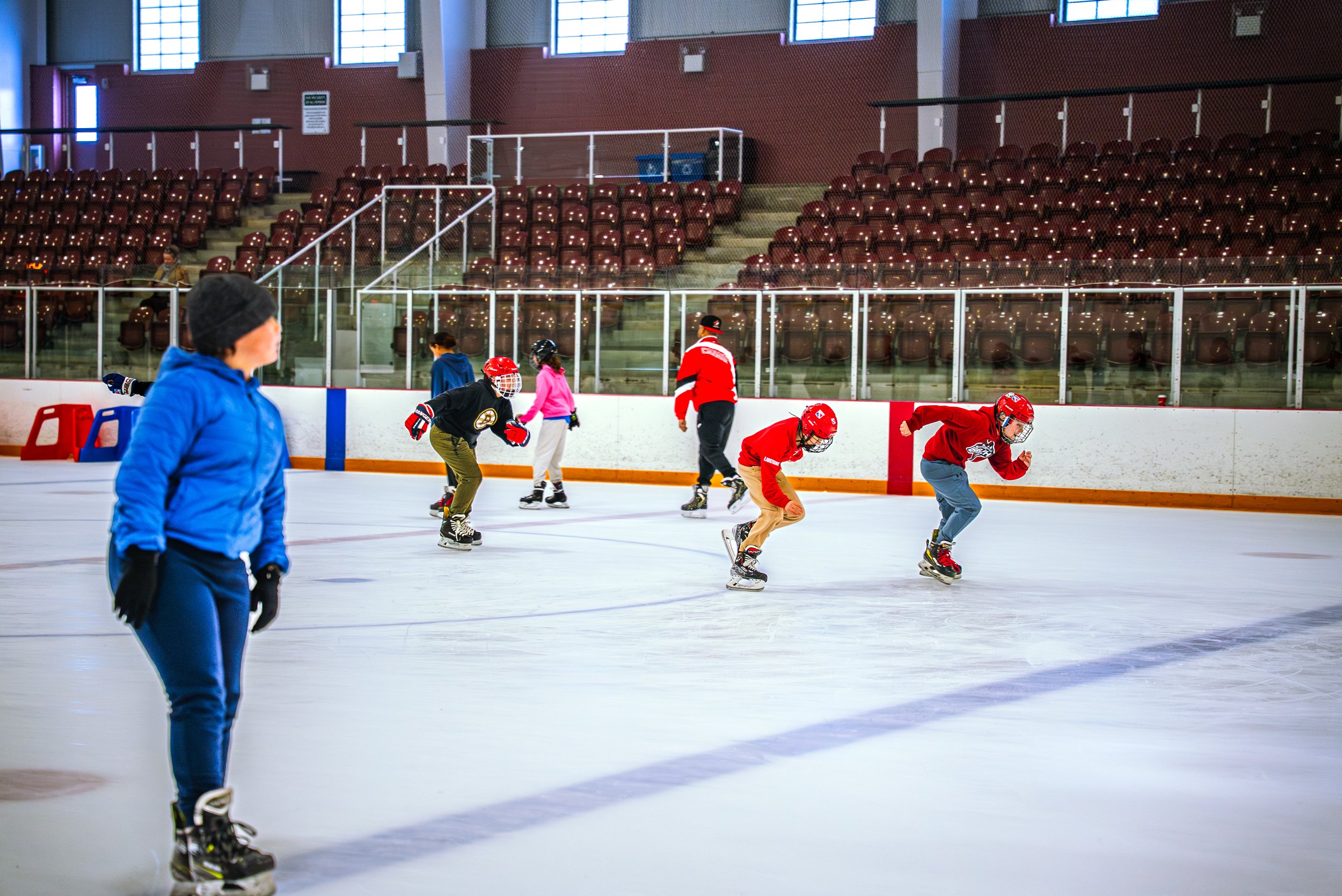 People ice skating at an indoor rink with empty stands in the background.