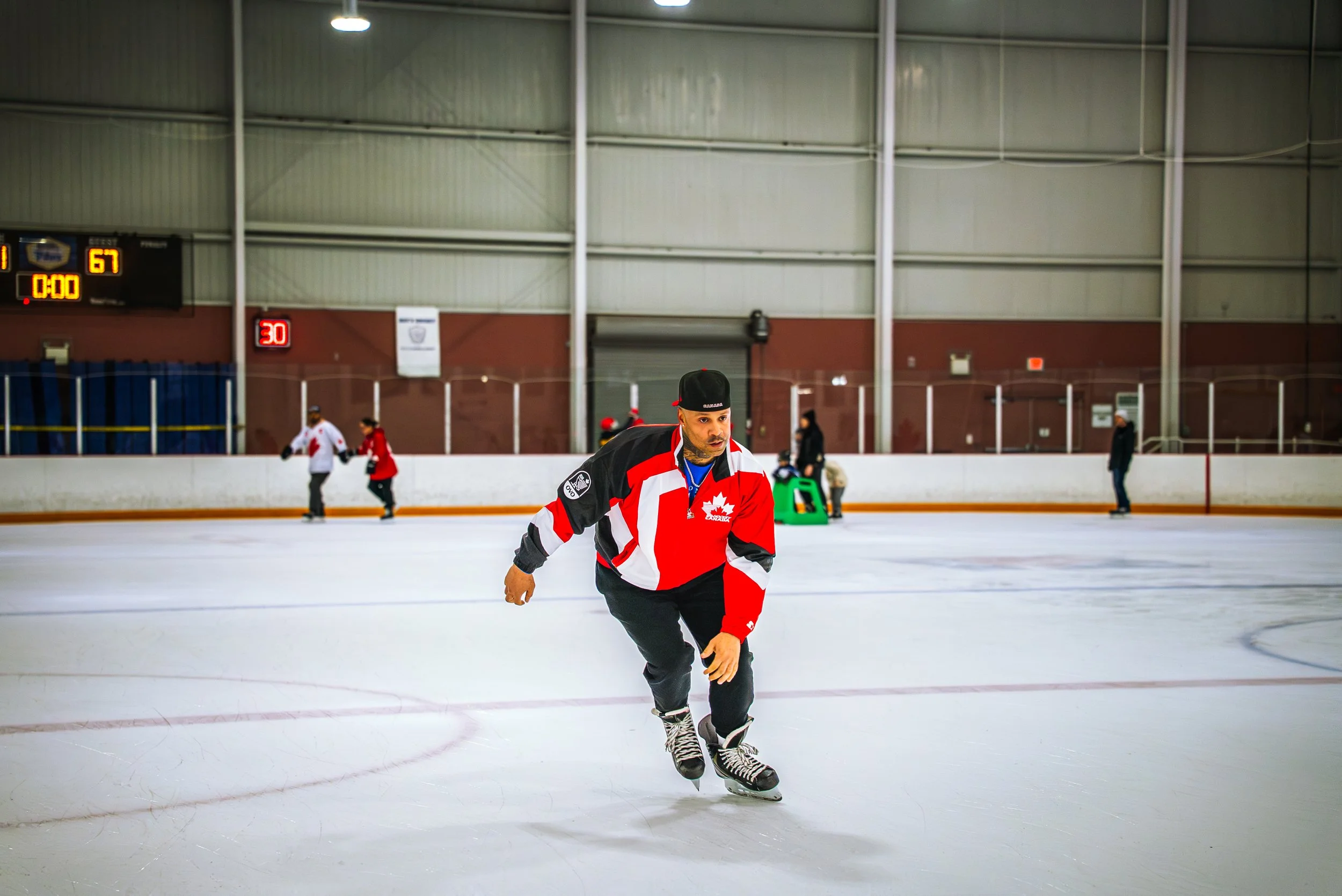 A person in a red, black, and white hockey jersey skating on an ice rink.