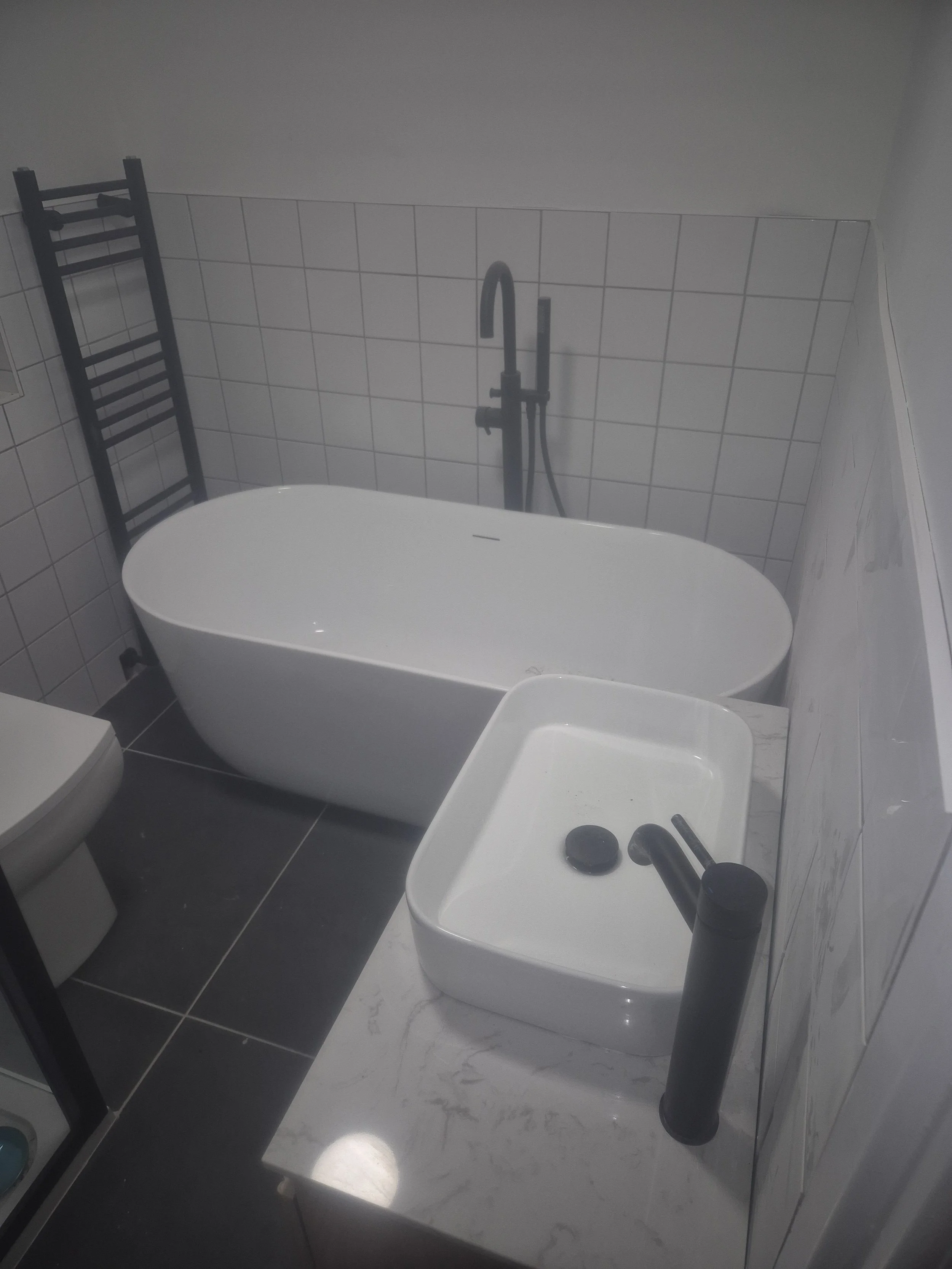 Bathroom with a white bathtub, a black towel rack, a sink with a black faucet, and tiled walls.
