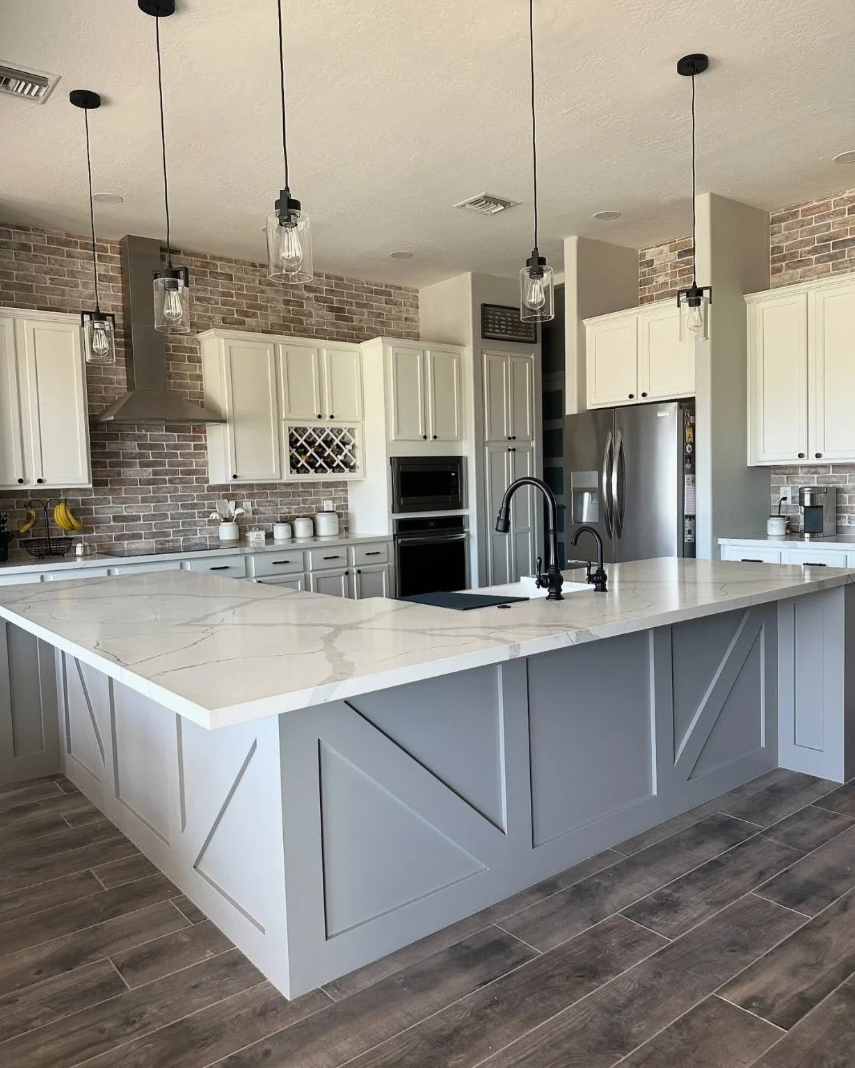 Kitchen remodeling project in Arizona featuring white cabinetry, a large island, black backsplash, stainless steel appliances, and pendant lighting.