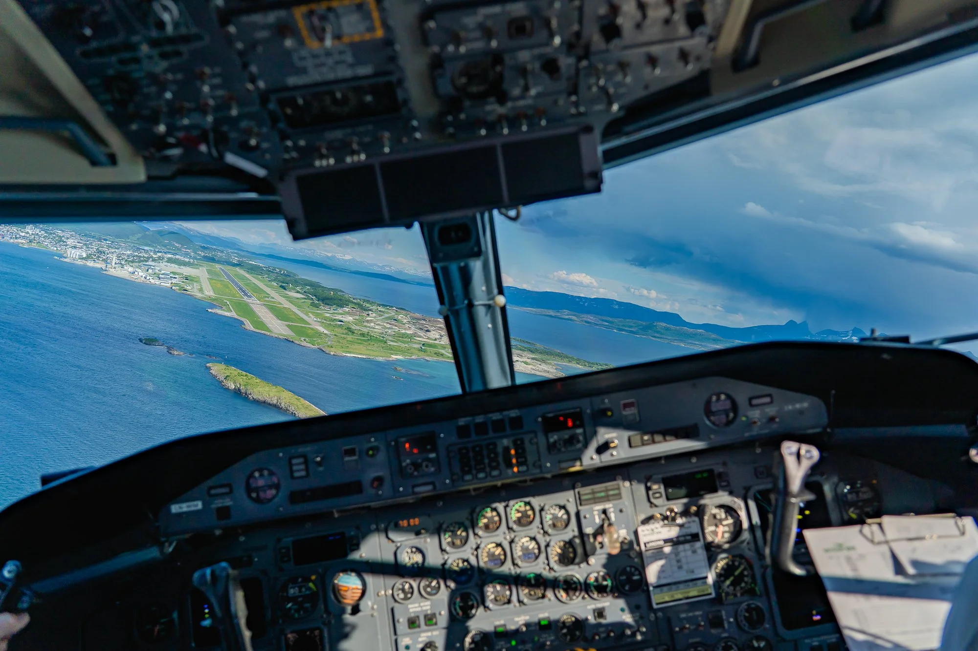 Het interieur van een vliegtuigcockpit met uitzicht op een eiland en water onder een gedeeltelijk bewolkte hemel.