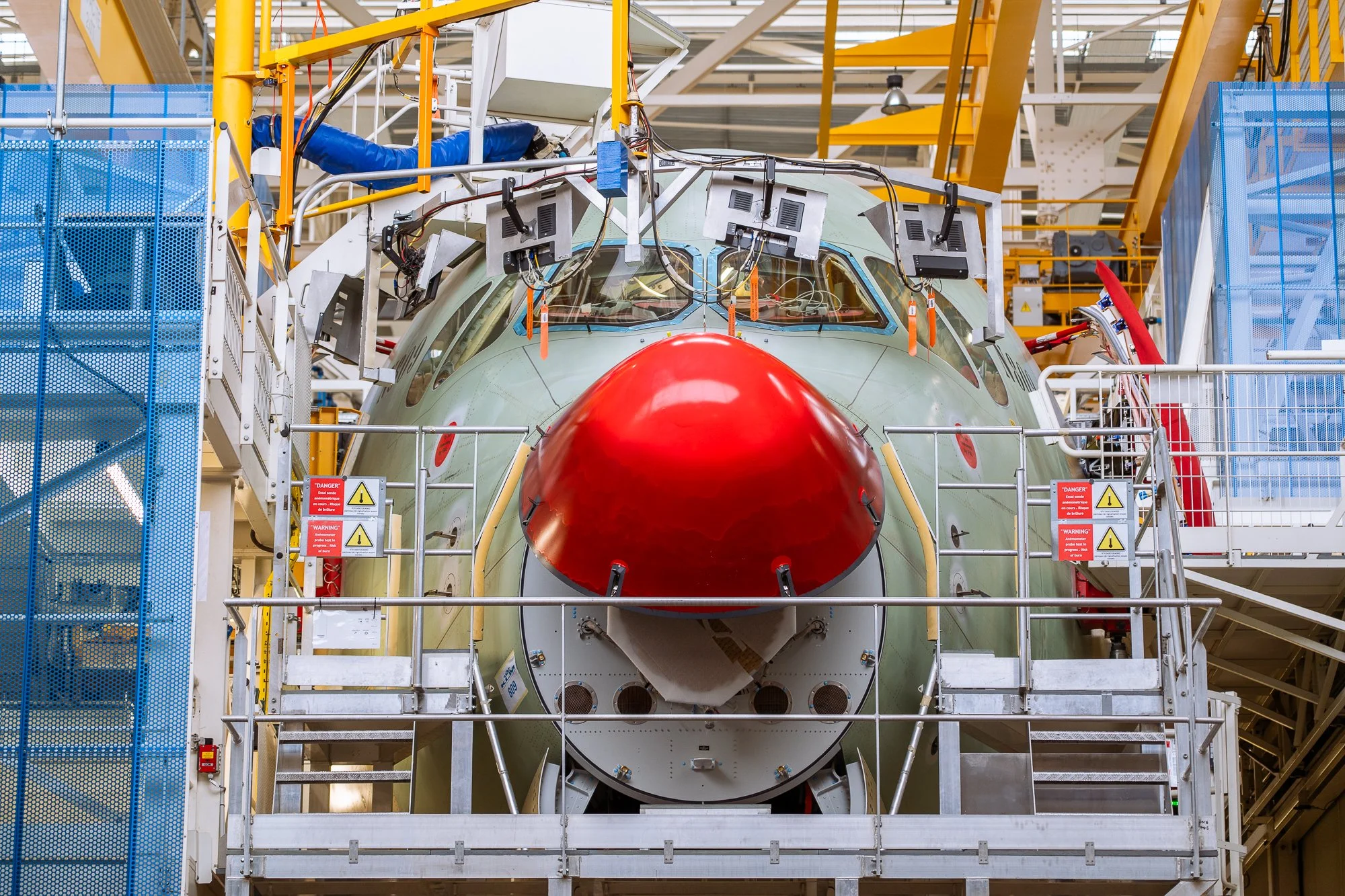 Vliegtuigcockpit onder constructie in een fabriek, omringd door staalramen en technologische apparatuur.
