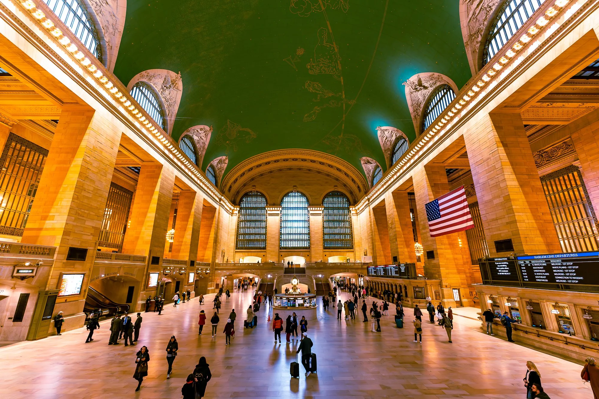 Binnenkant van een groot treinstation met mensen die wachten, een Amerikaanse vlag en informatieborden.